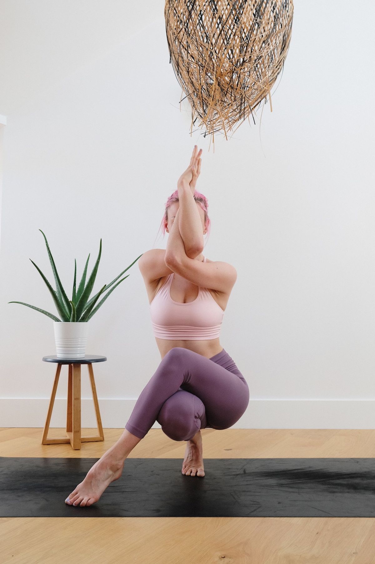 Yoga teacher balancing in eagle pose beside a plant