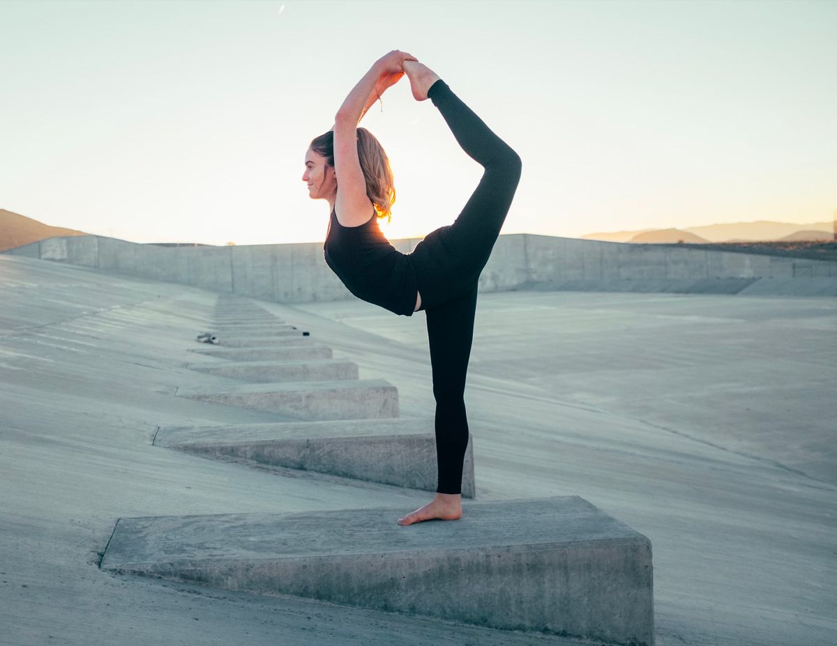 Yoga teacher stretching one leg high outdoors