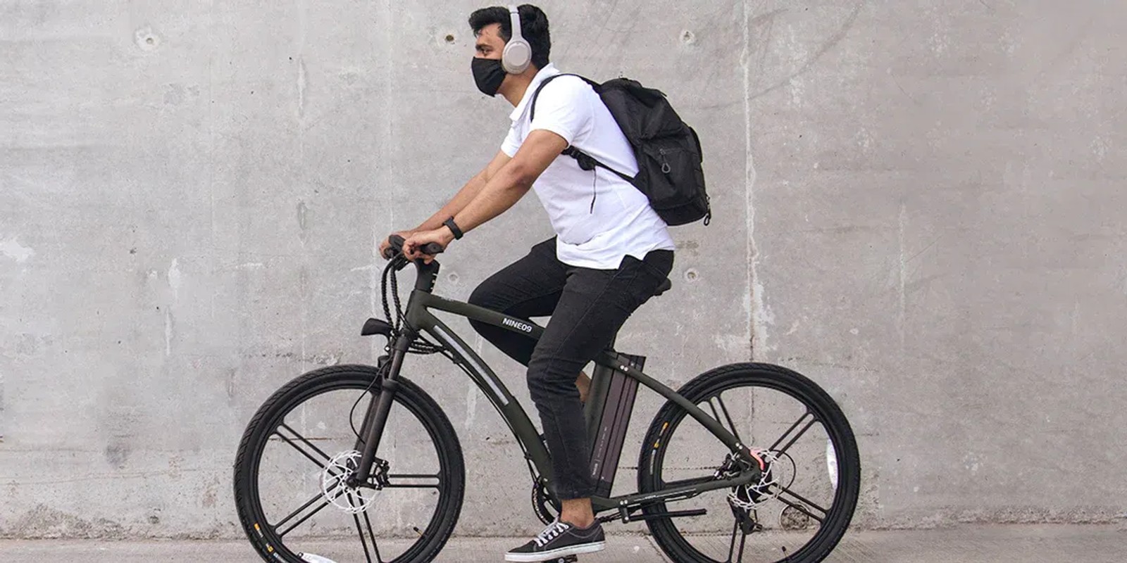 Commuter riding a NINE09 electric bike past a concrete wall, showing everyday eBike use in the city