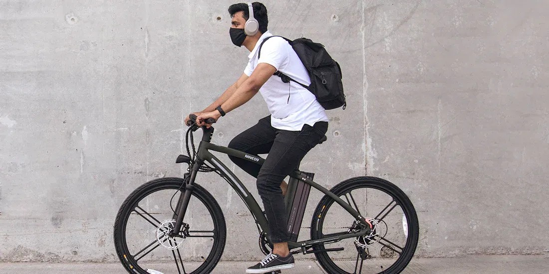 Commuter riding a NINE09 electric bike past a concrete wall, showing everyday eBike use in the city