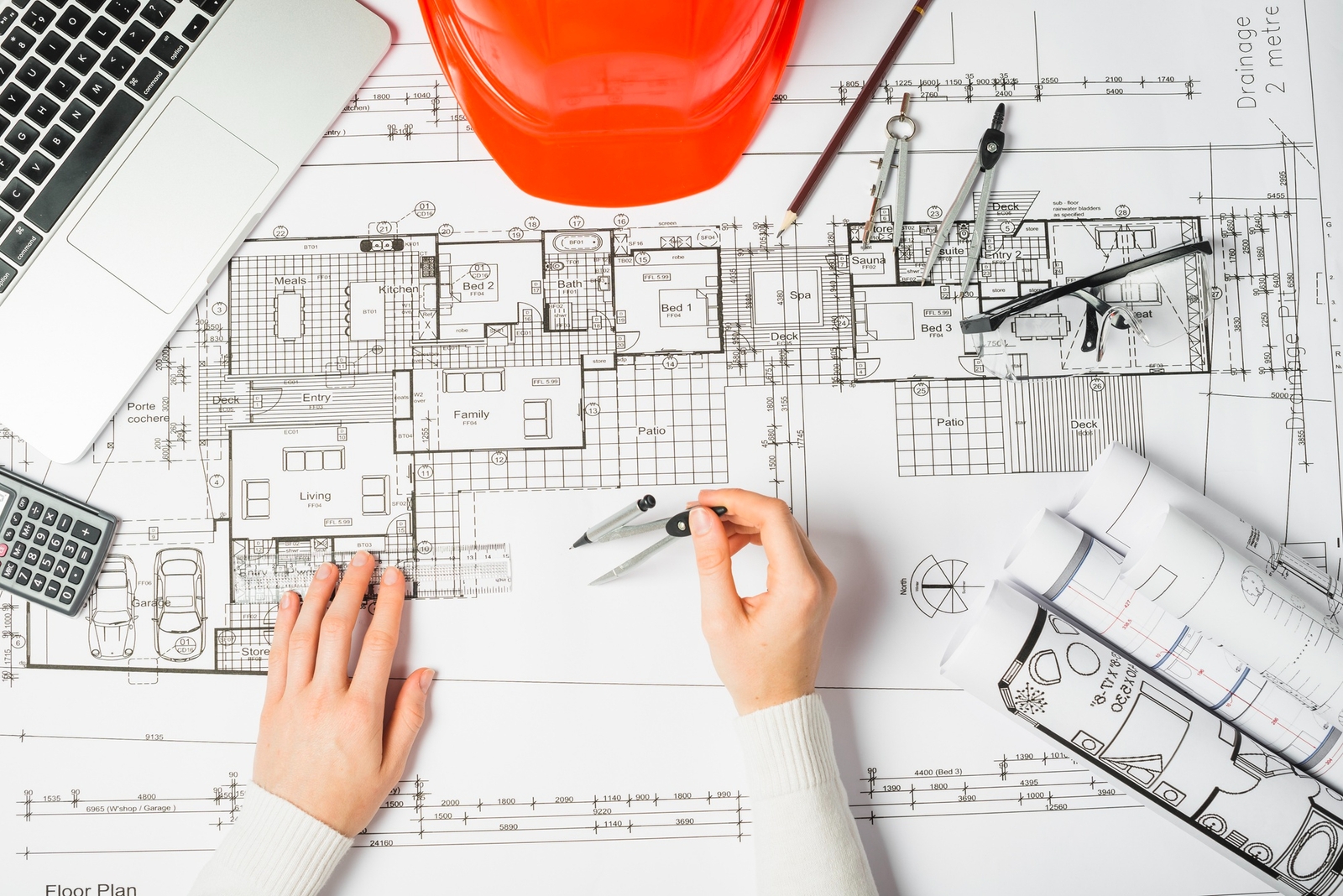 Photo of hands drafting a detailed floor plan blueprint with drafting compass and tools