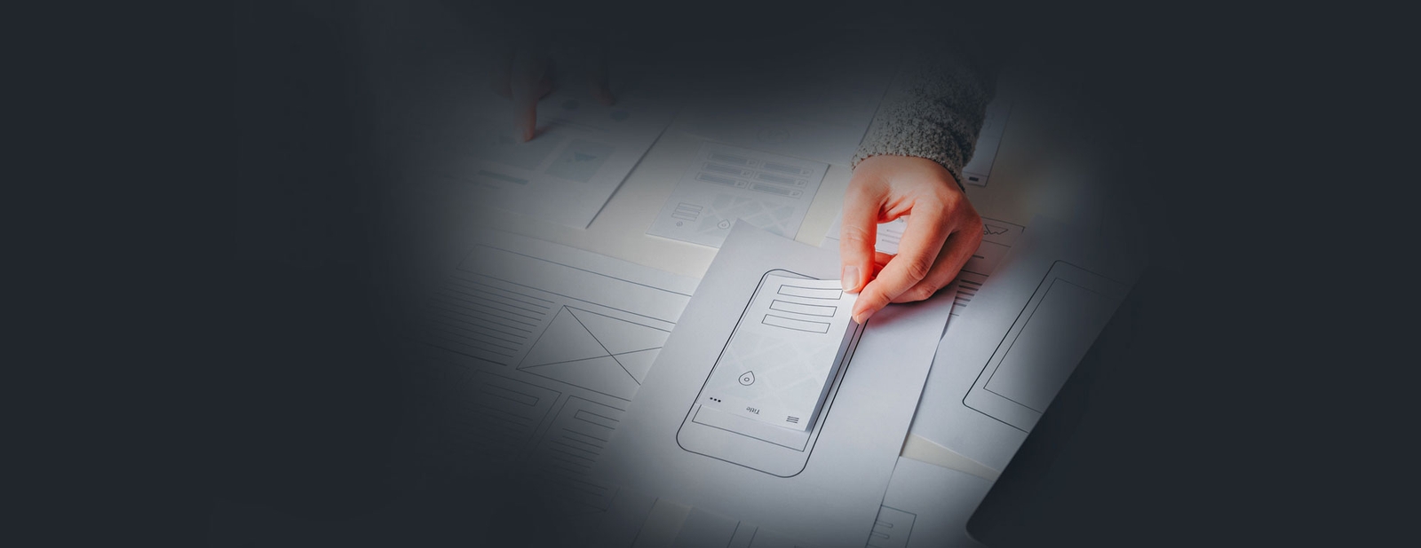 Flutter Web Development Photo of hands arranging paper wireframe sketches of a mobile app interface on a table
