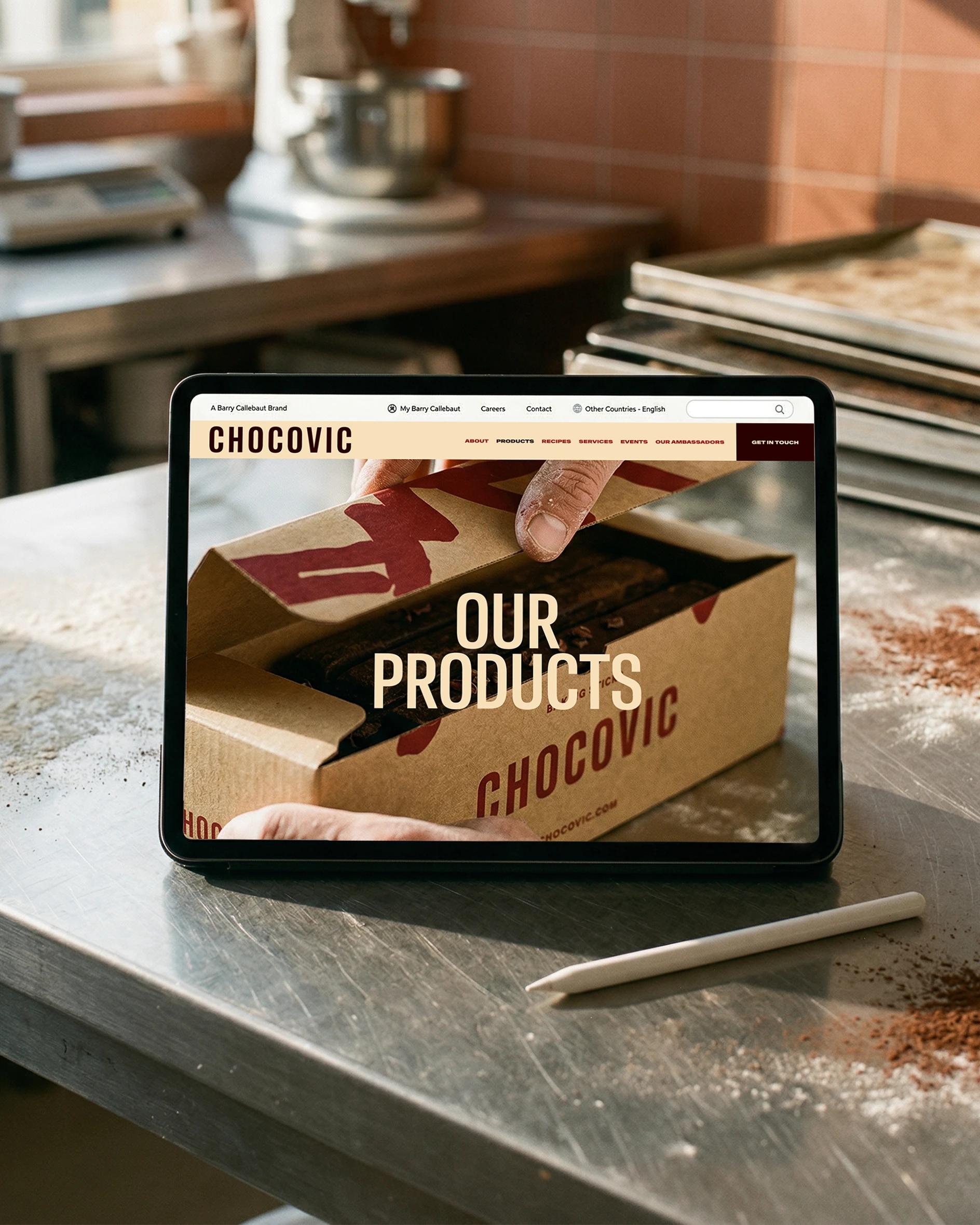 Chocovic — stacked Chocovic baking-stick boxes with the brush pattern, beside the website on a tablet on a bakery bench 2