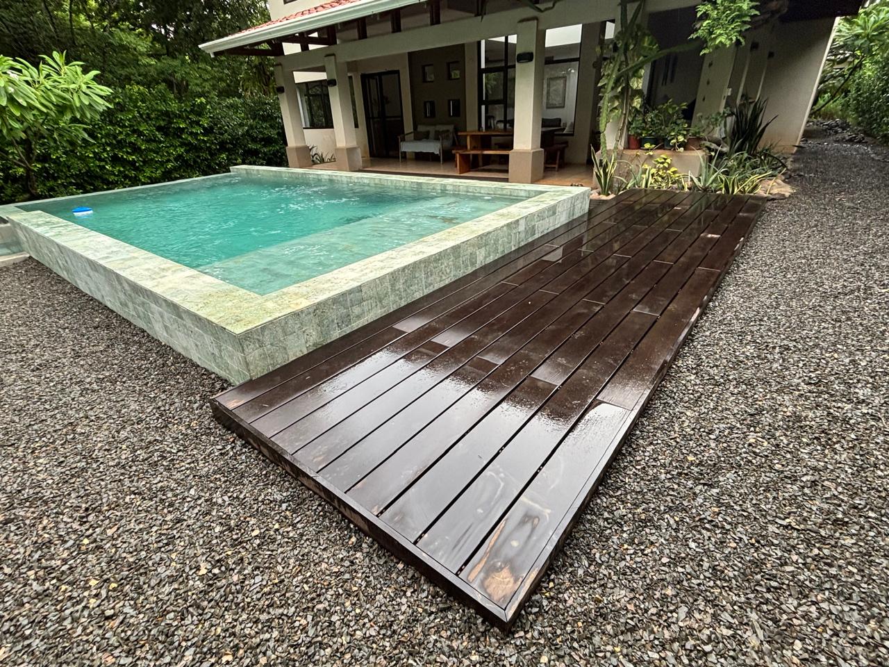 Piscina elevada en piedra verde con muro, deck de madera y jardín