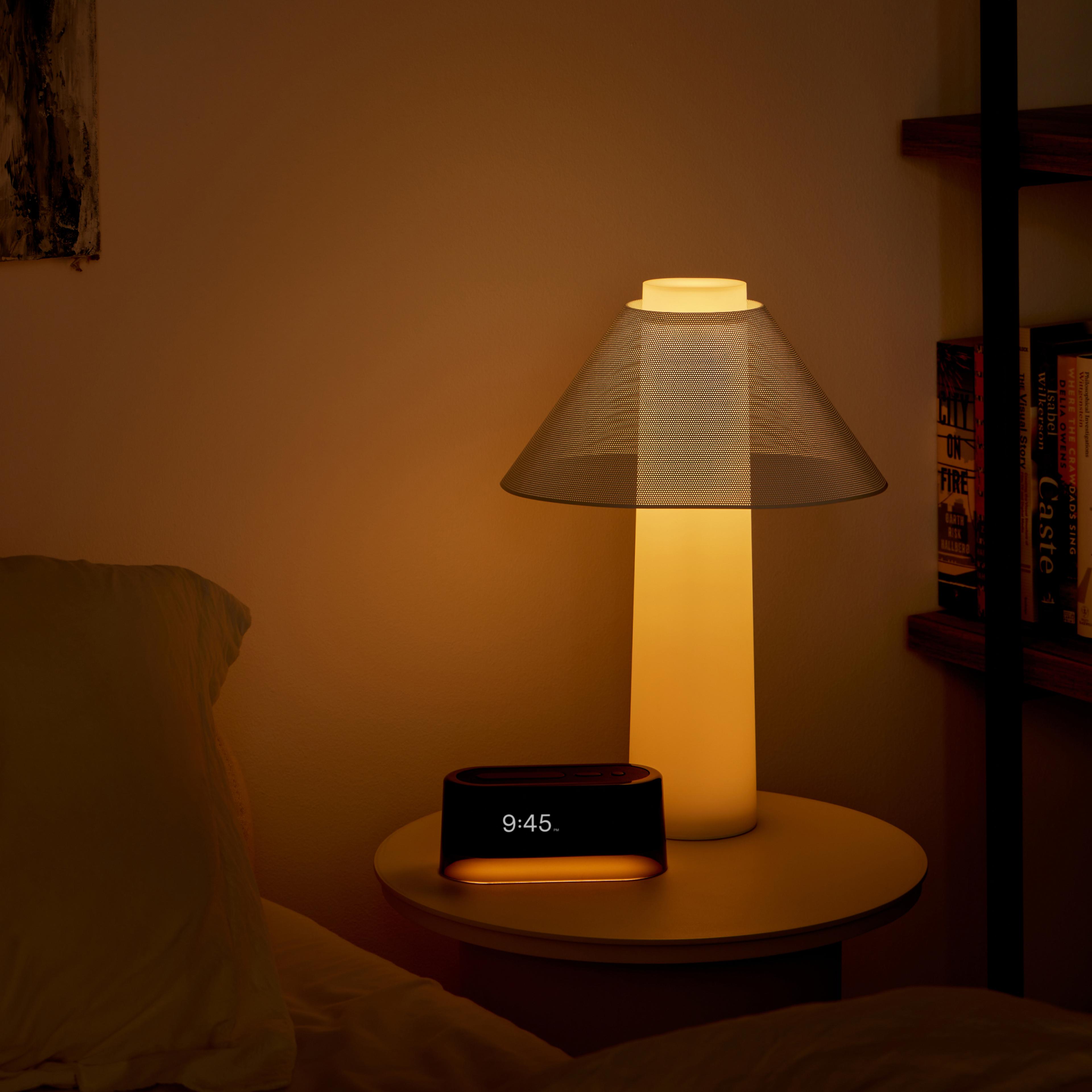 A warm-lit bedroom scene with a bedside table, a modern lamp, and a glowing digital alarm clock showing 9:45.