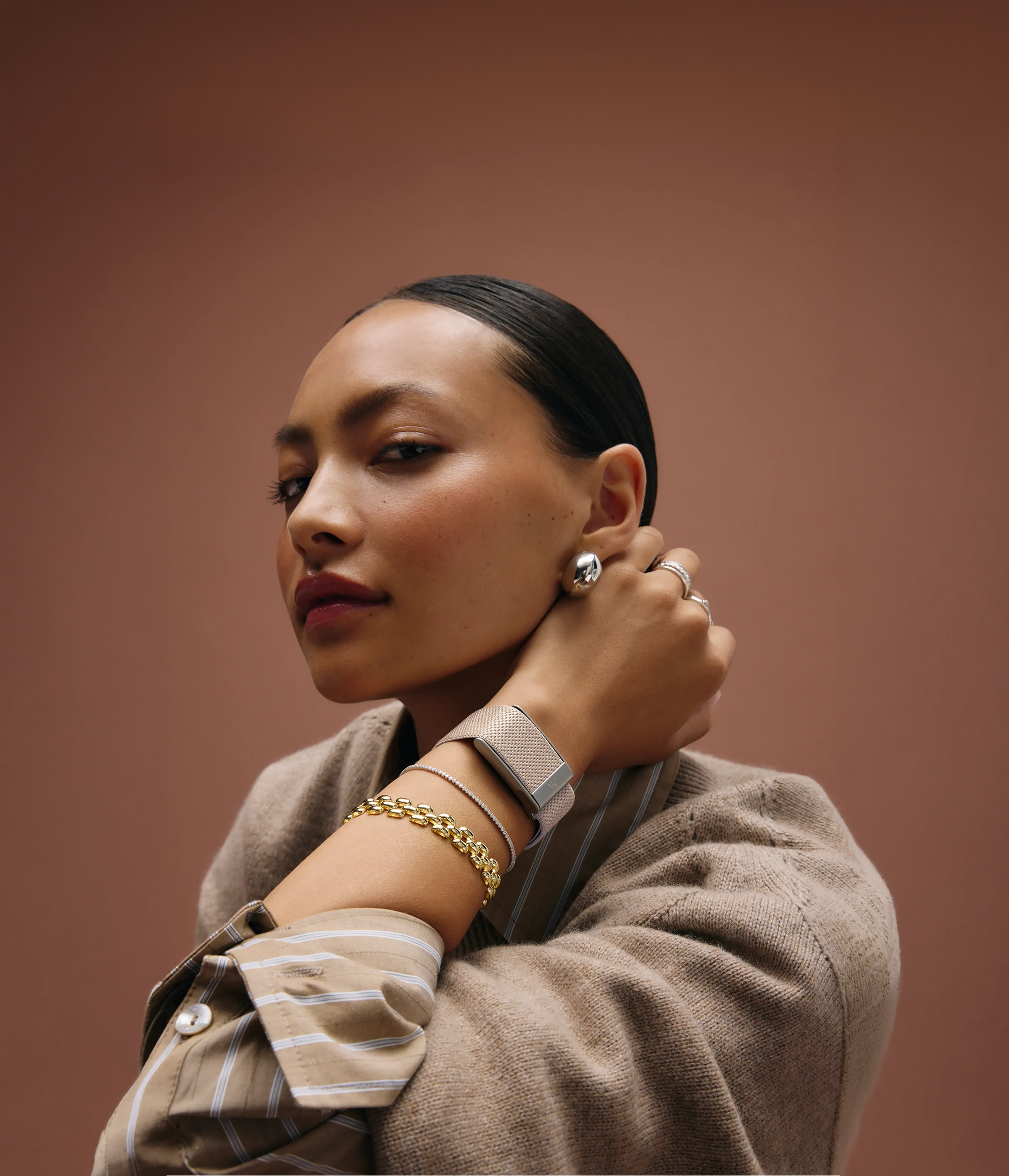 A woman wearing a WHOOP in a silver SuperKnit Luxe strap against a sepia backdrop.