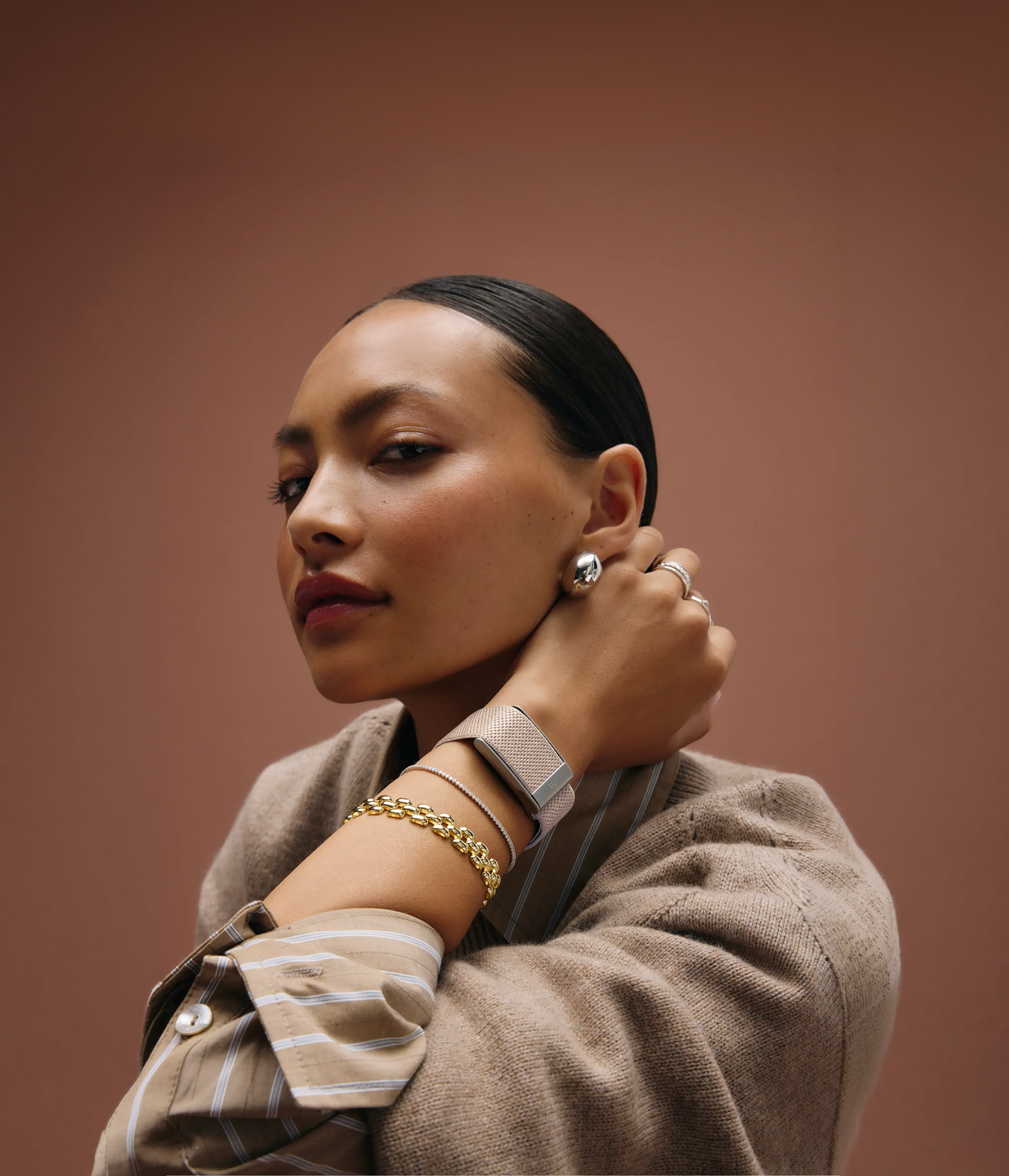 A woman wearing a WHOOP in a silver SuperKnit Luxe strap against a sepia backdrop.