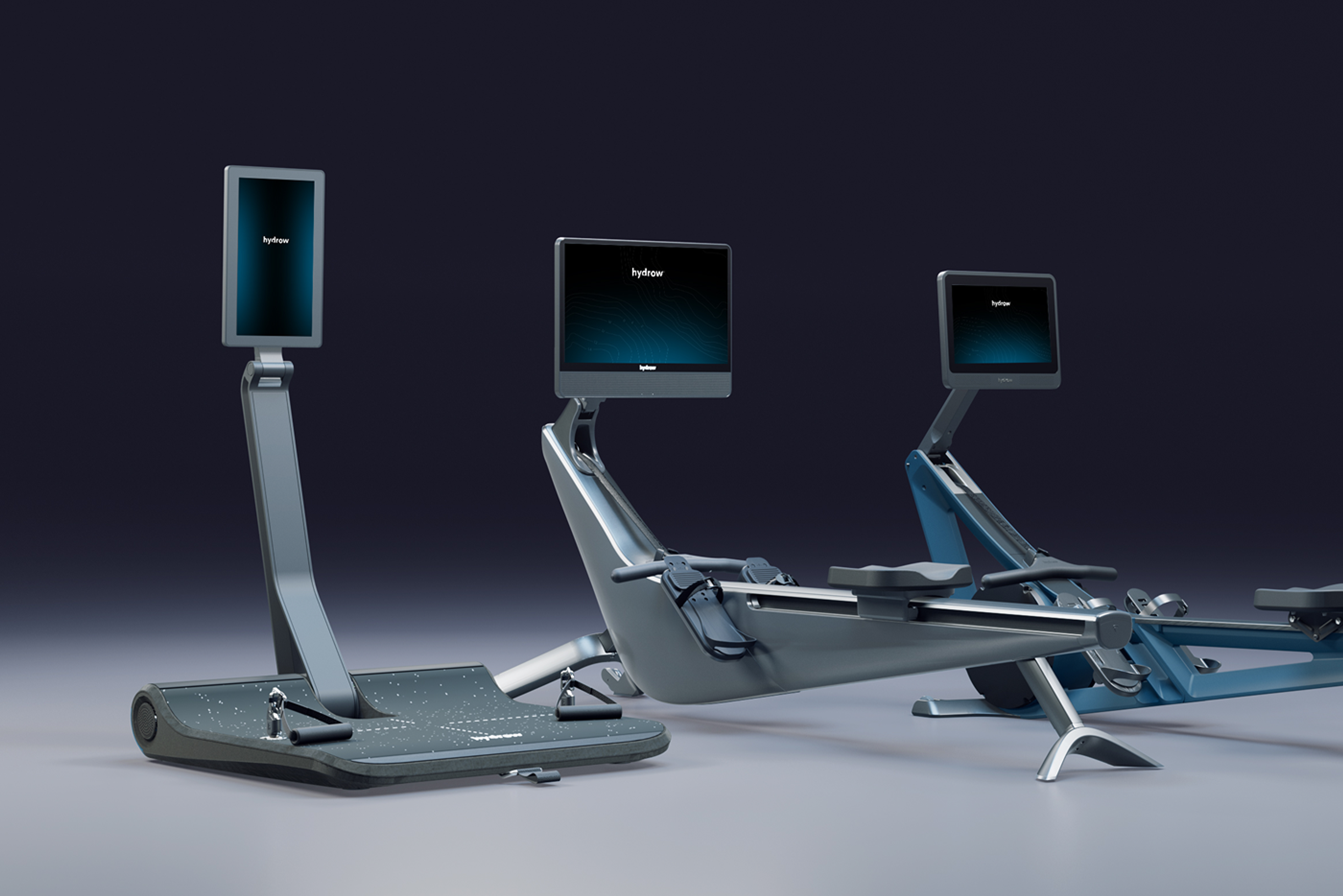 Three modern Hydrow exercise machines: a standing workout platform and two rowing machines, all with digital displays.