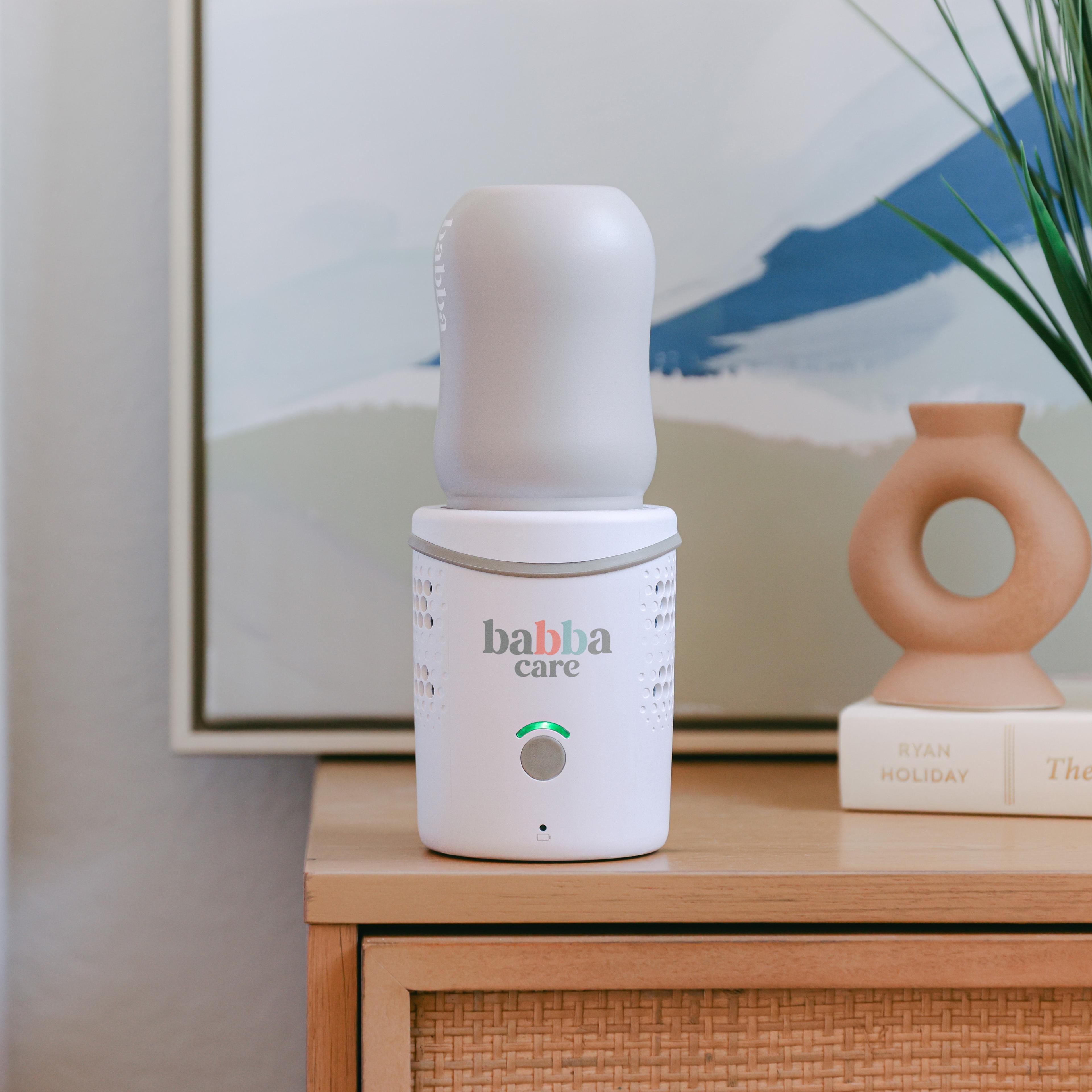 A white Babba Care baby formula maker sits on a wooden nightstand with decorative items in the background.