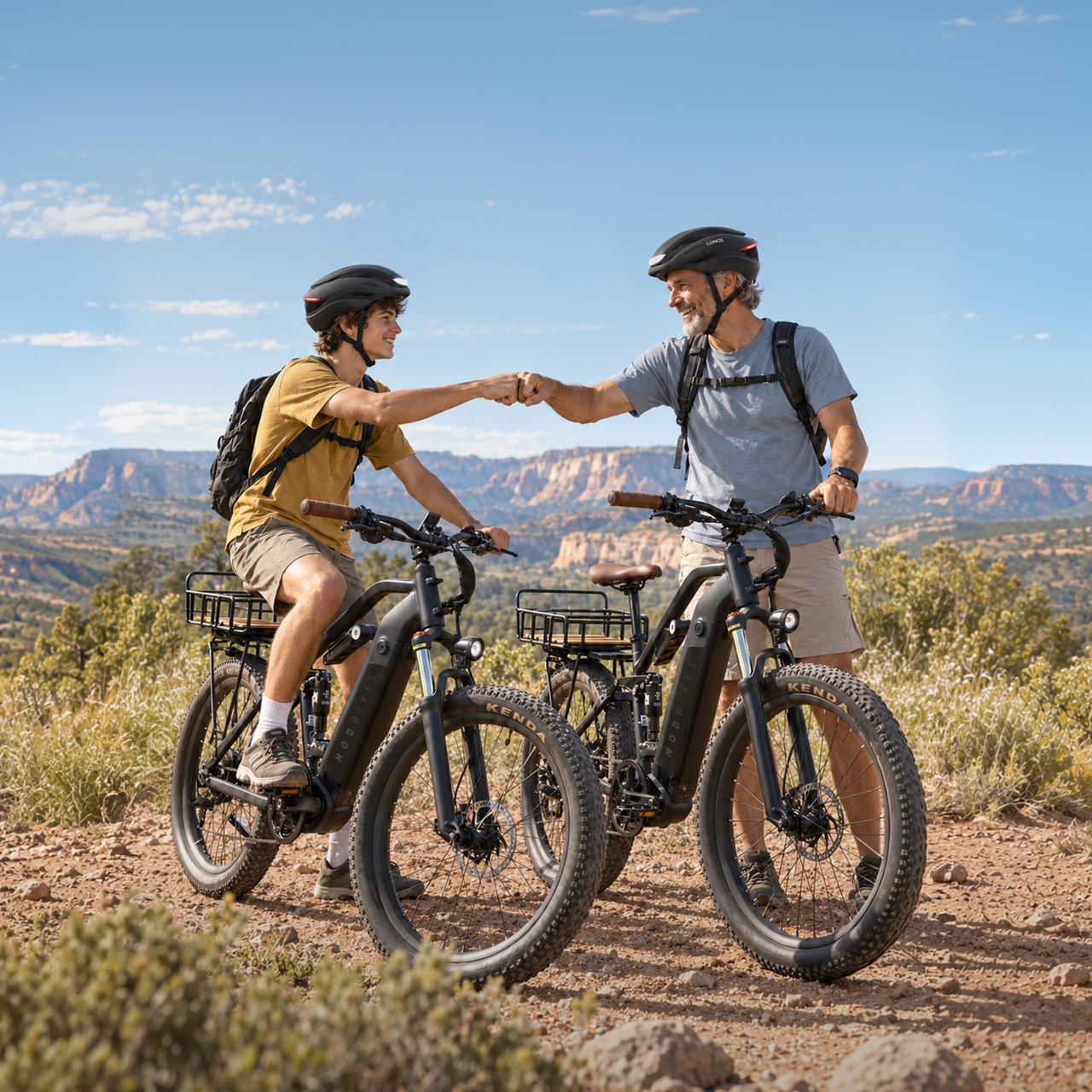 Two men on electric bikes fist bump on a scenic trail overlooking a canyon.