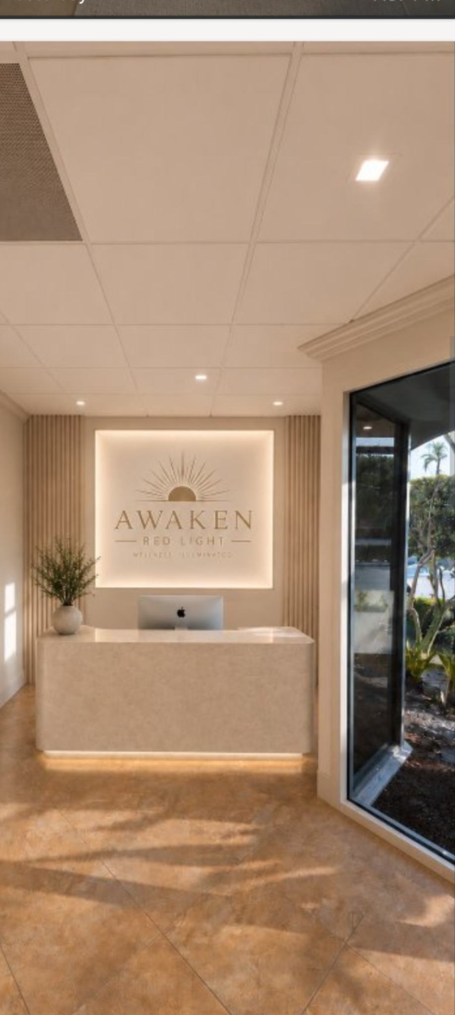 A modern reception area with a curved desk, an iMac, and a backlit "AWAKEN RED LIGHT" sign.