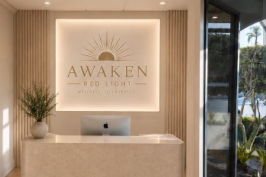 A modern reception area with a curved desk, an iMac, and a backlit "AWAKEN RED LIGHT" sign.