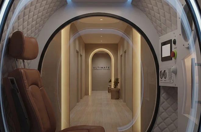View from inside a futuristic pod with a brown leather chair, looking out to a hallway that says "Ultimate Longevity Center."