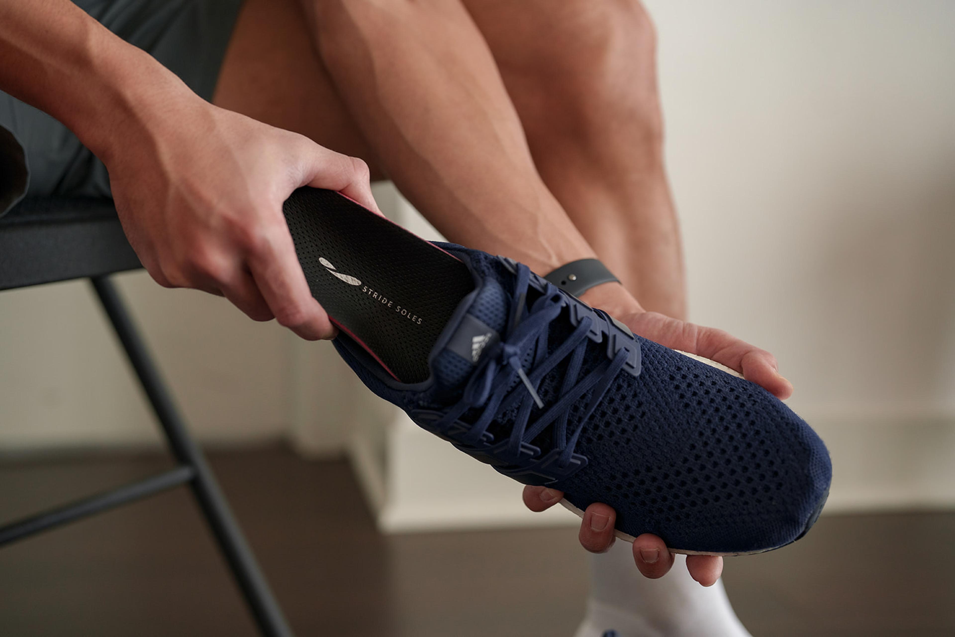 Person inserting a "STRIDE SOLES" insole into a navy blue athletic shoe.