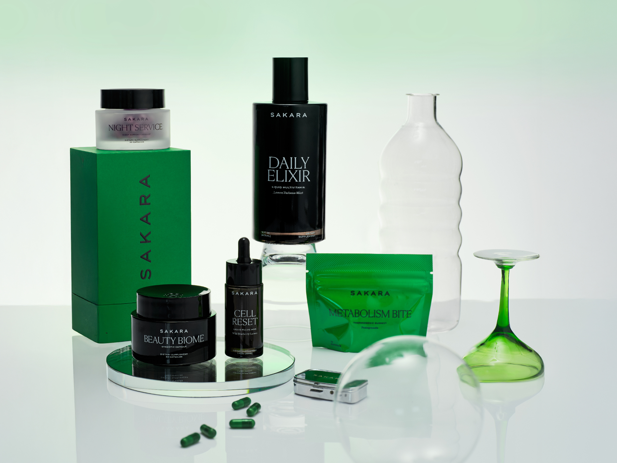 Sakara wellness and beauty products in black and green packaging, displayed with decorative glass.
