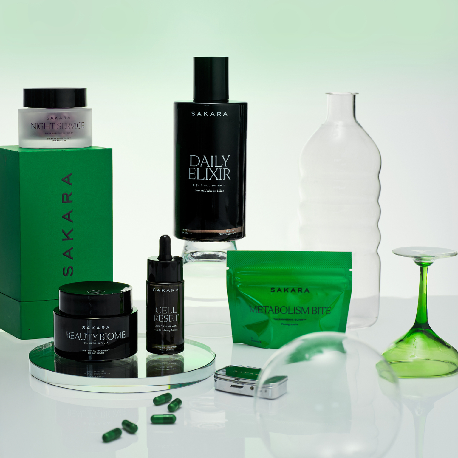 Sakara wellness and beauty products in black and green packaging, displayed with decorative glass.