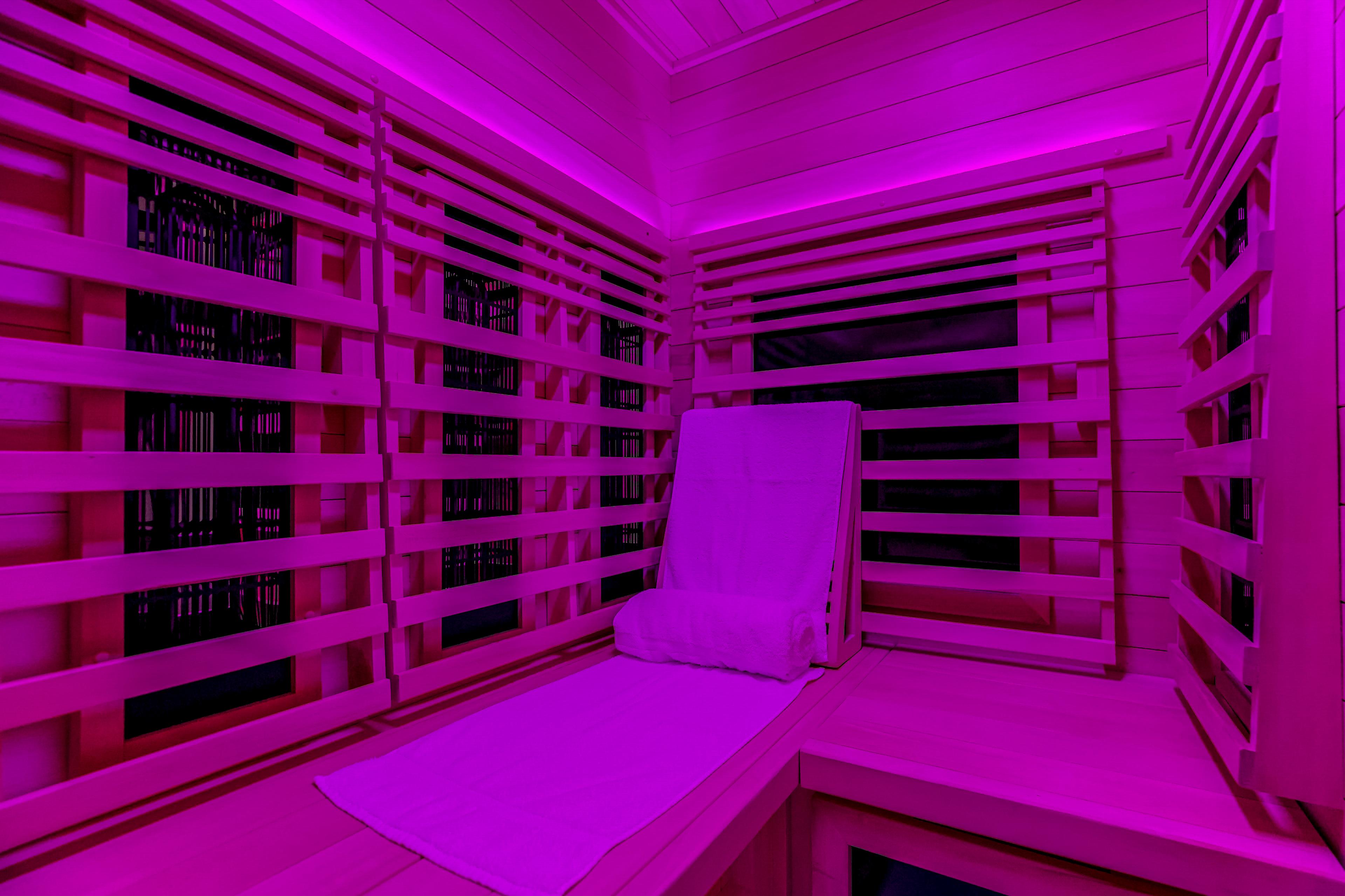 Vibrant purple-lit wooden infrared sauna with a white towel on a bench.