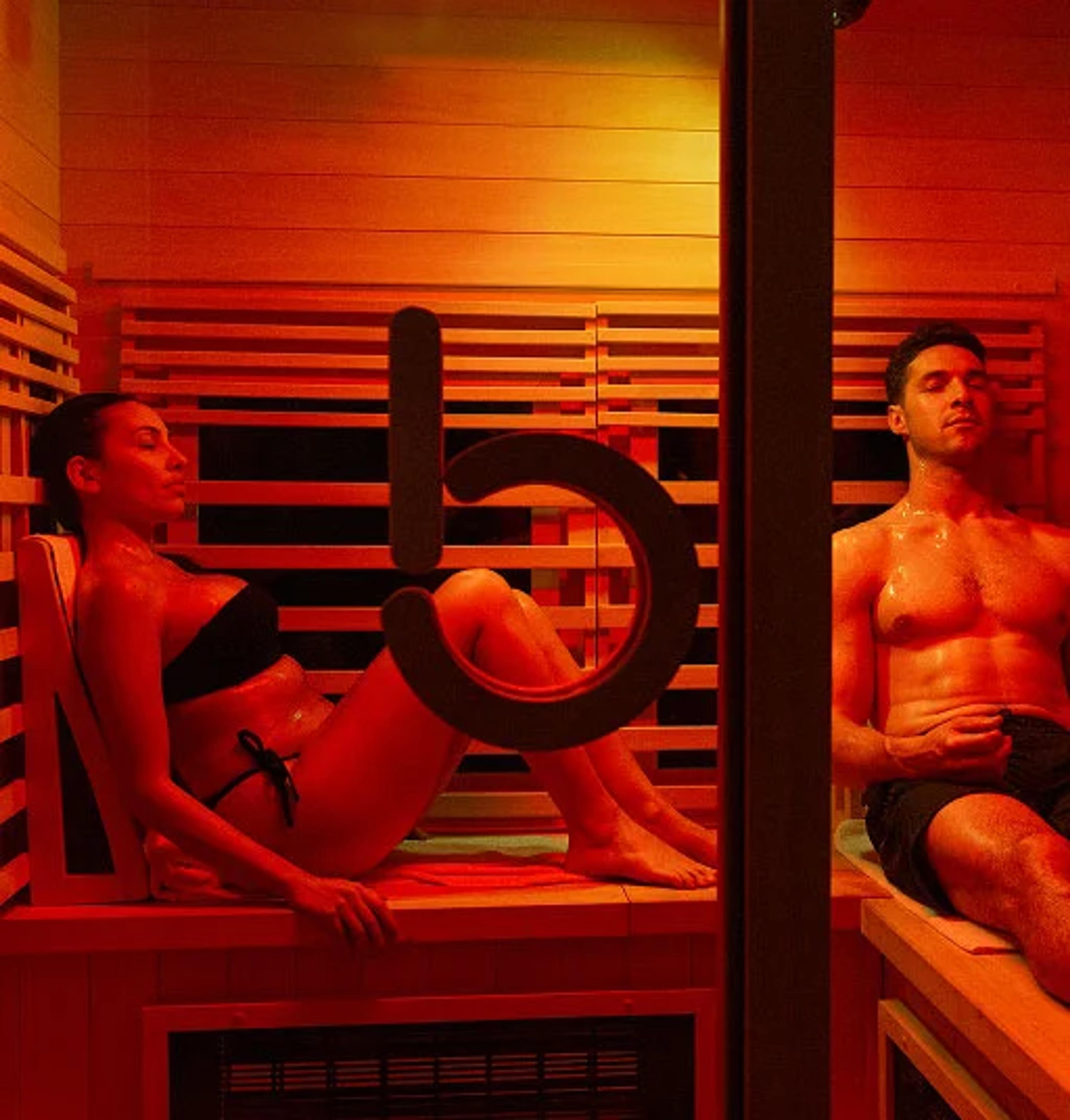 A man and woman sweating in a red-lit sauna.
