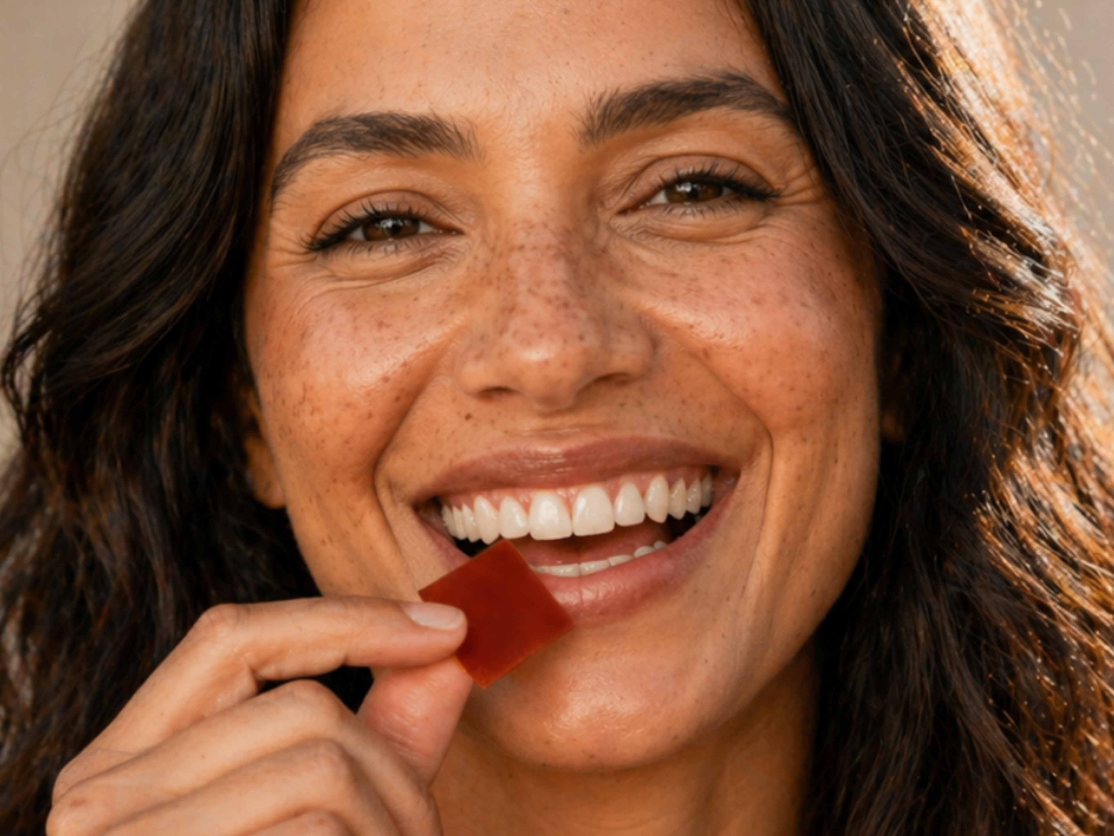 A smiling woman holding a red square chewable to her mouth.