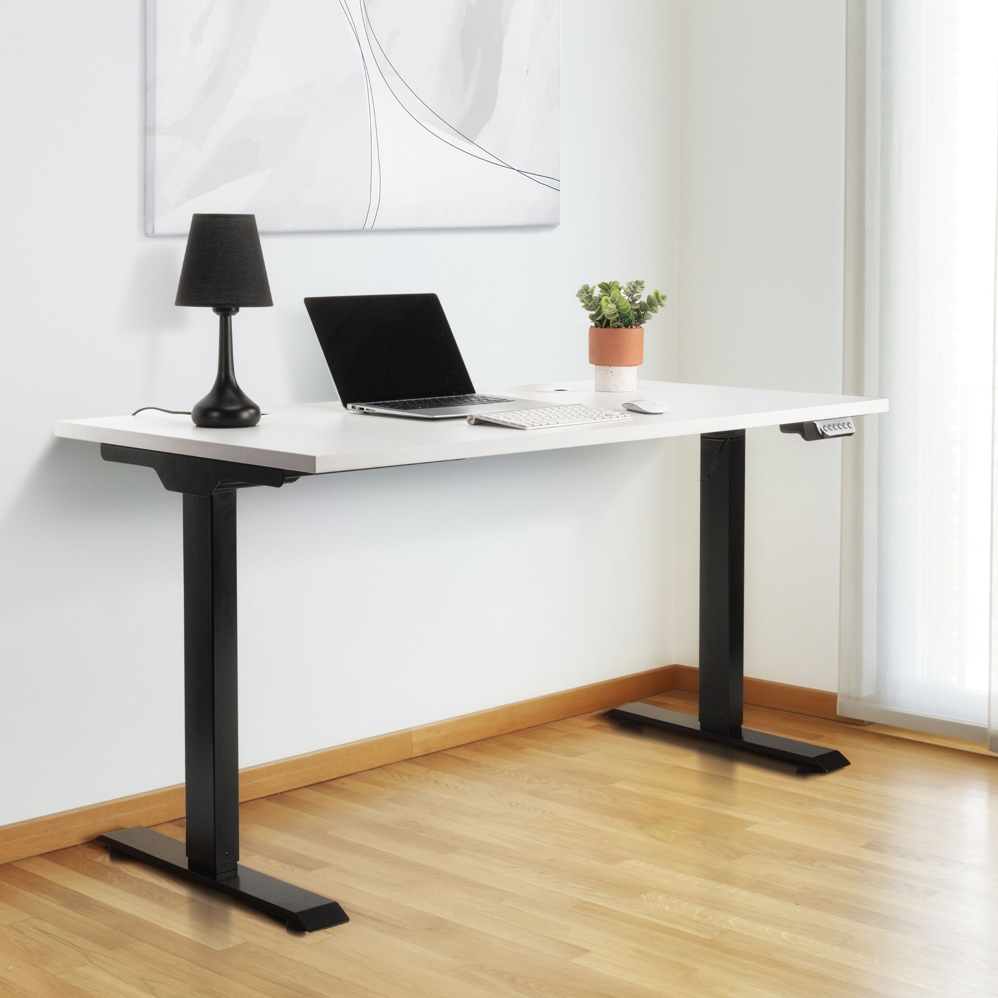 White standing desk with black legs, laptop, black lamp, and potted plant.