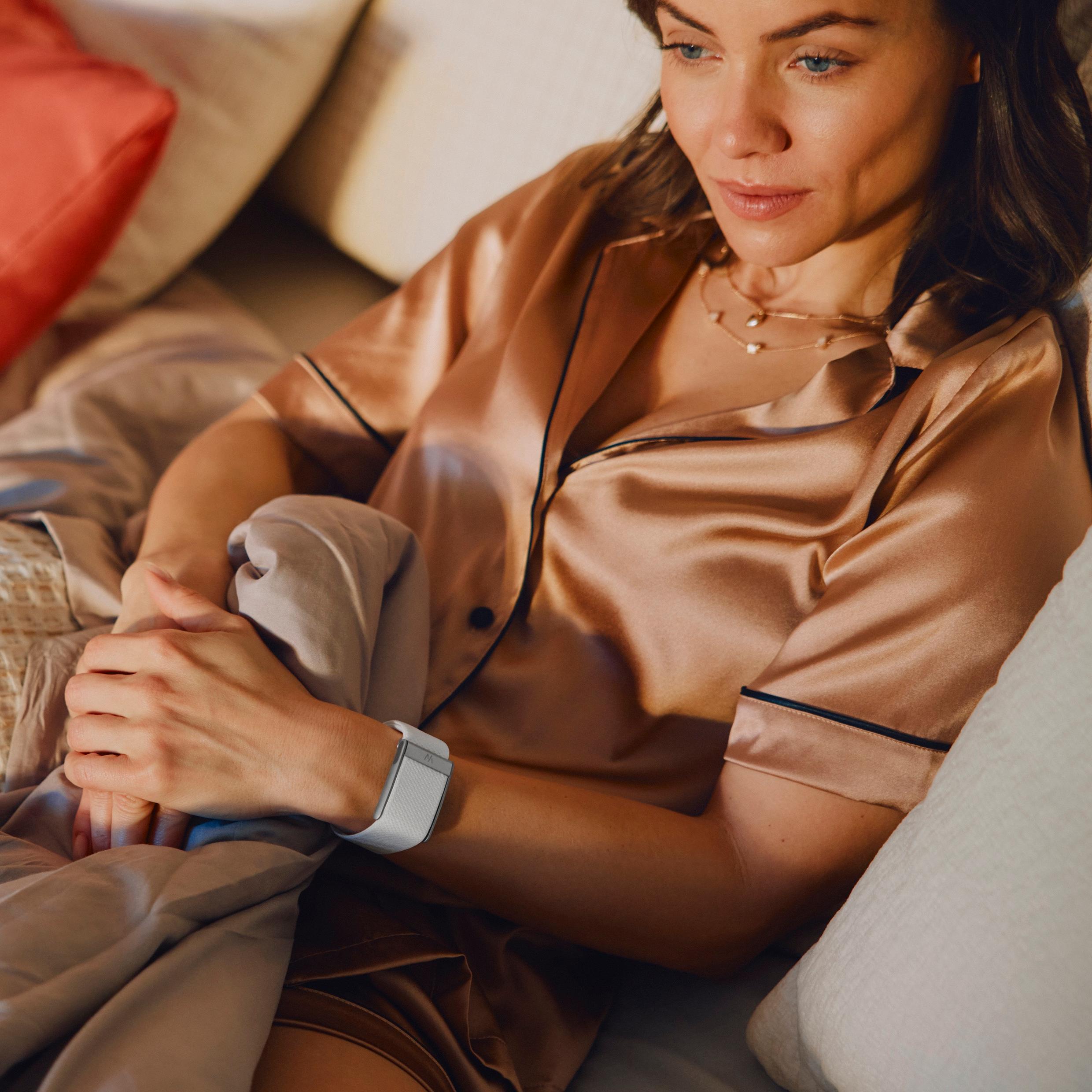A woman in silk pajamas with a WHOOP sits pensive in bed.