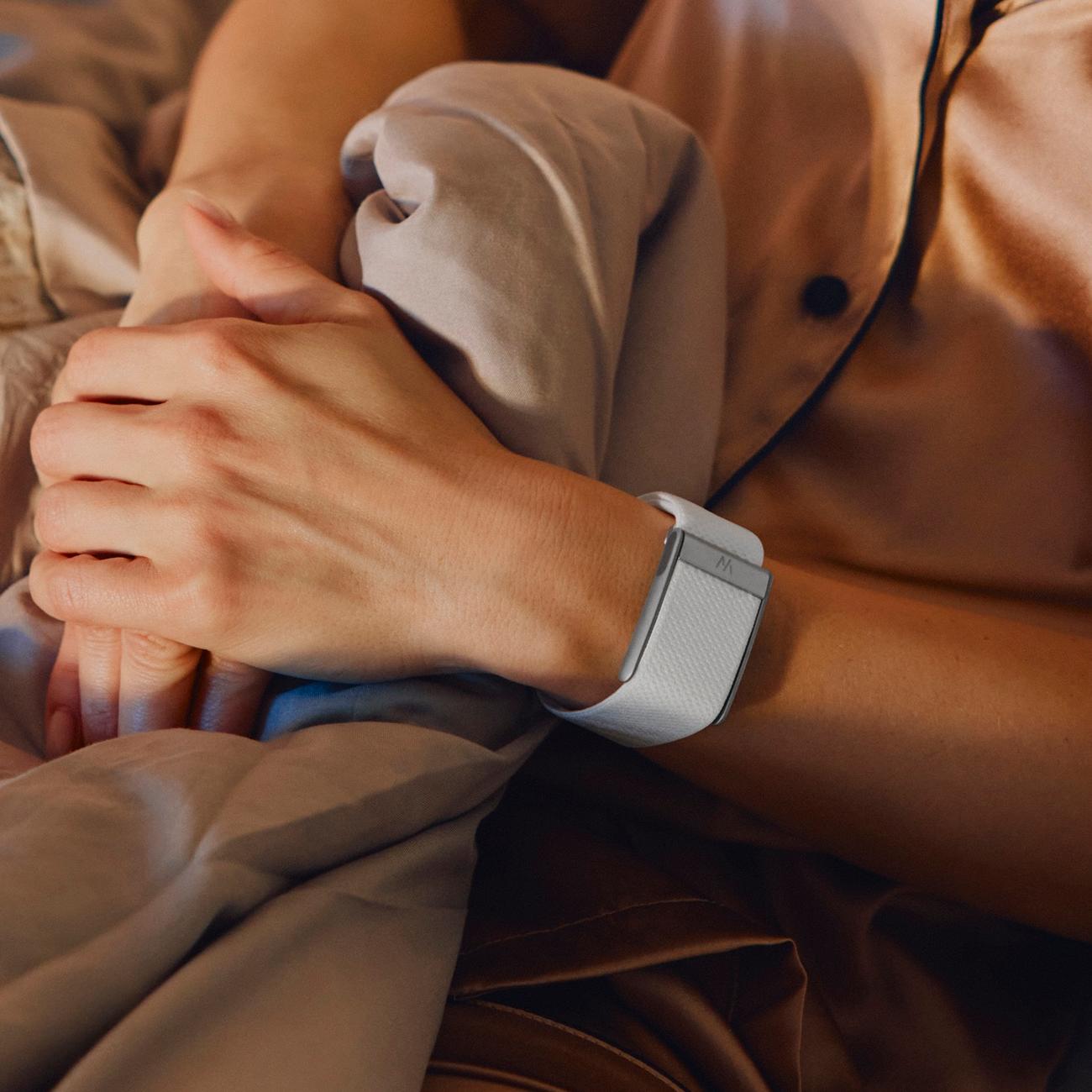 Close-up of a WHOOP worn on the wrist, hands resting on bedding.