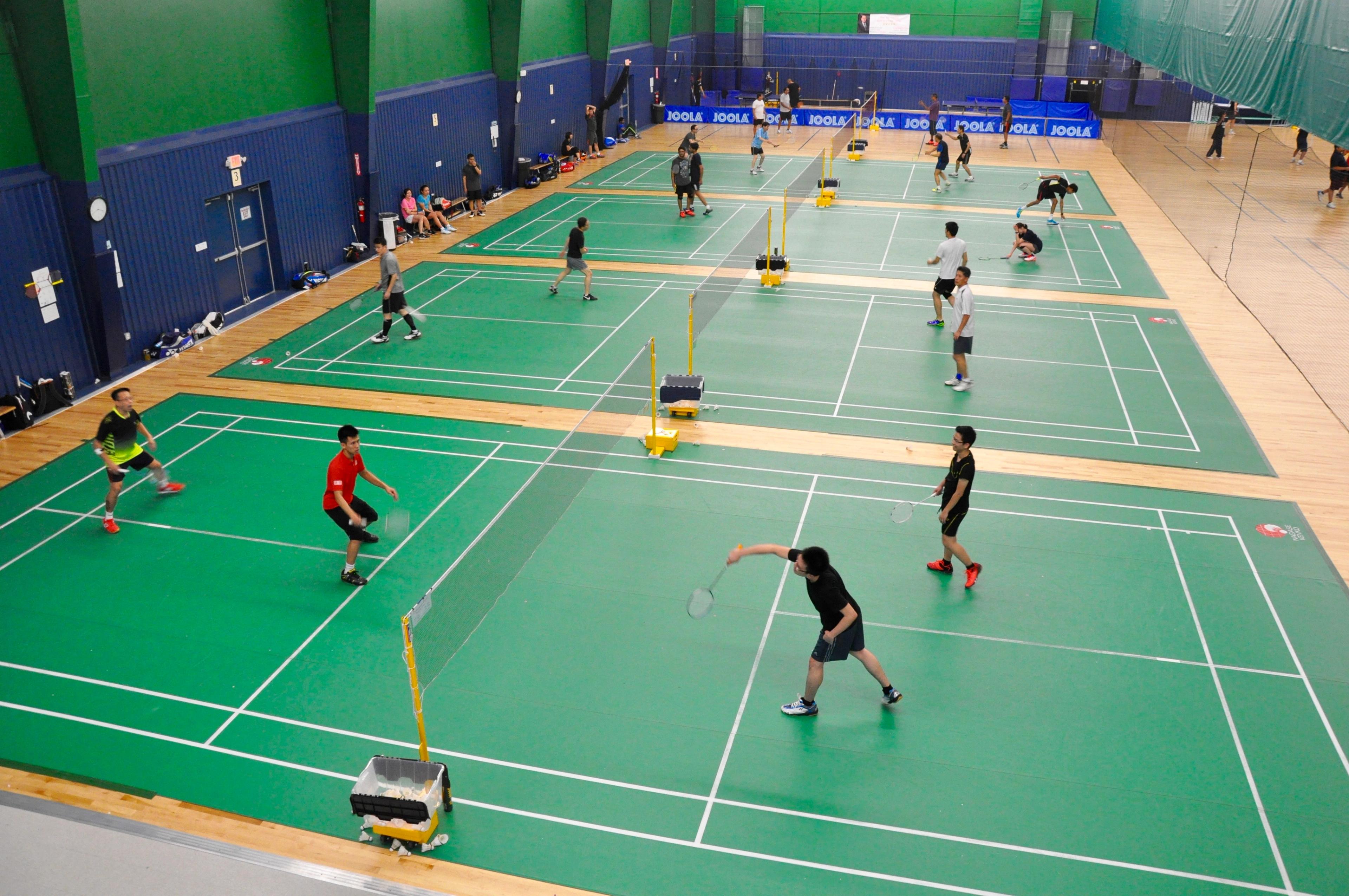 People playing badminton on multiple courts in an indoor facility.