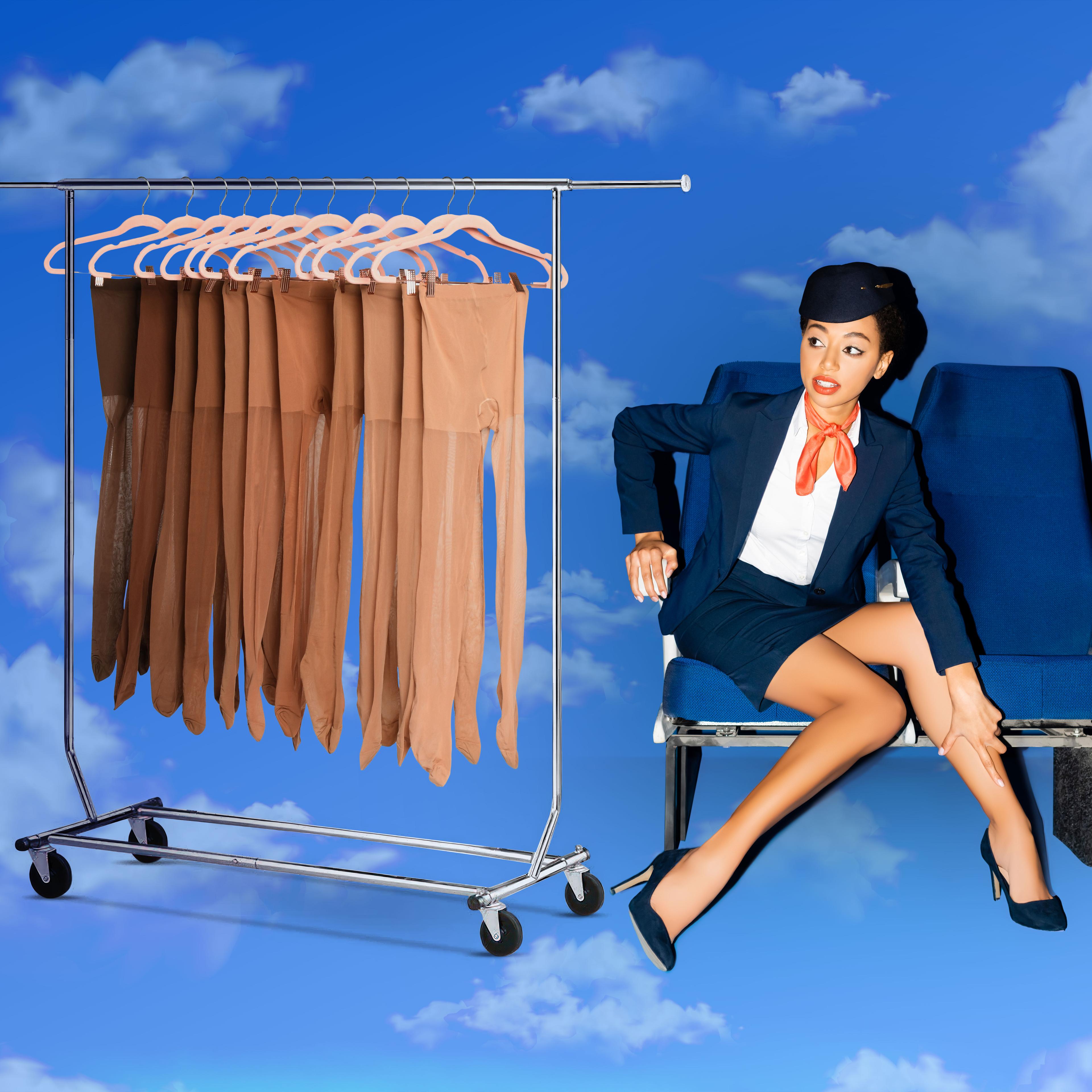 A flight attendant adjusts her leg next to a rack of pantyhose, sitting on airplane seats against a cloudy sky.