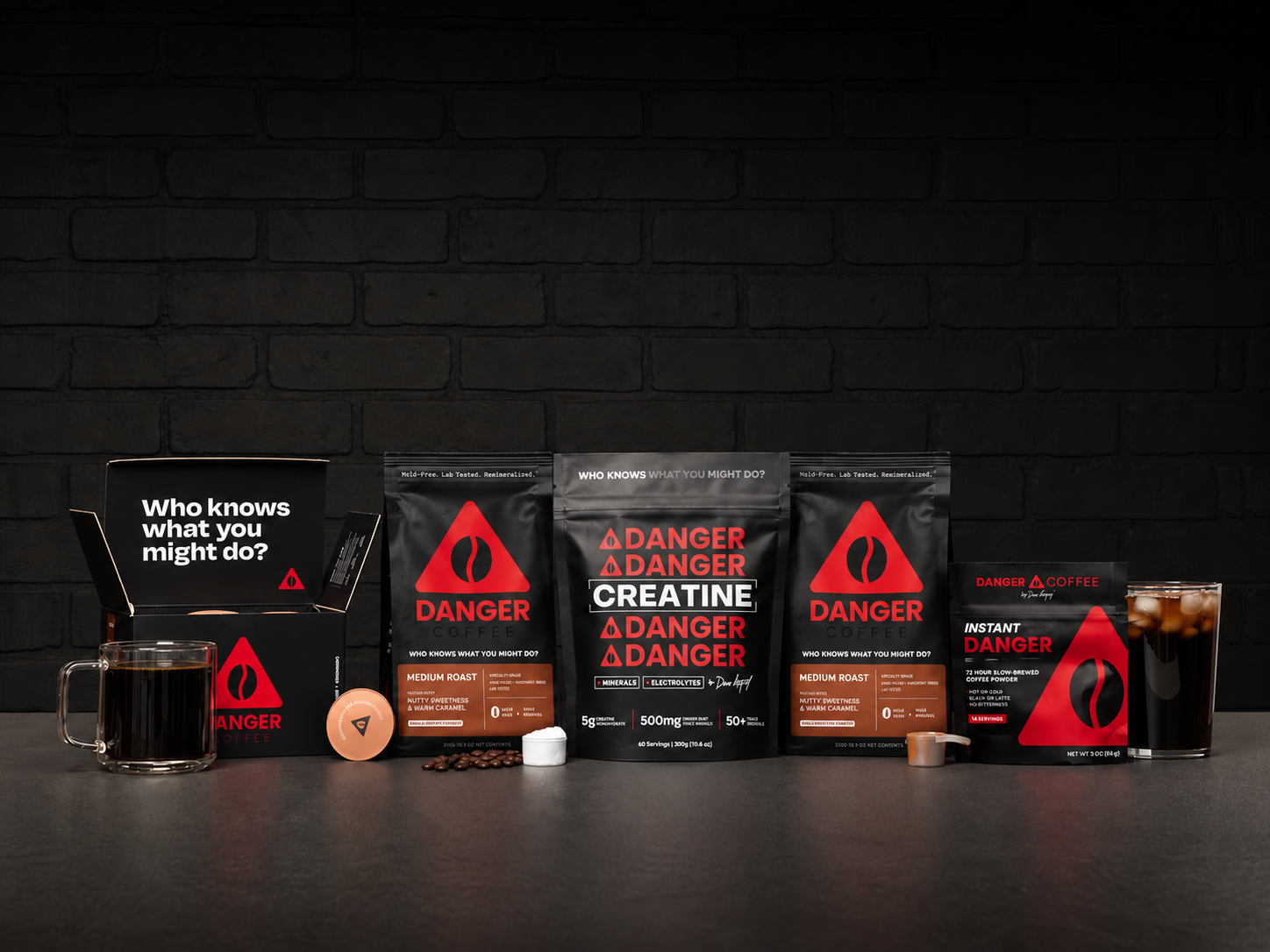 A collection of black and red Danger Coffee products, including bags of ground coffee, creatine coffee, instant coffee, coffee pods, a mug of hot coffee, and a glass of iced coffee.