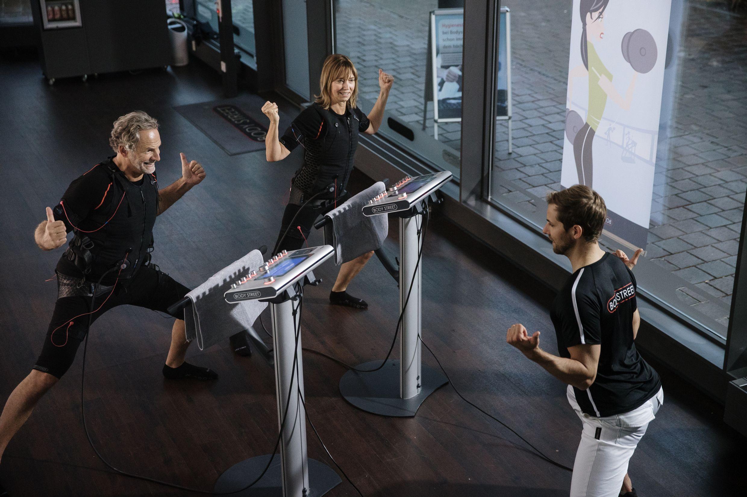 Two adults in EMS training suits exercising with a male instructor.