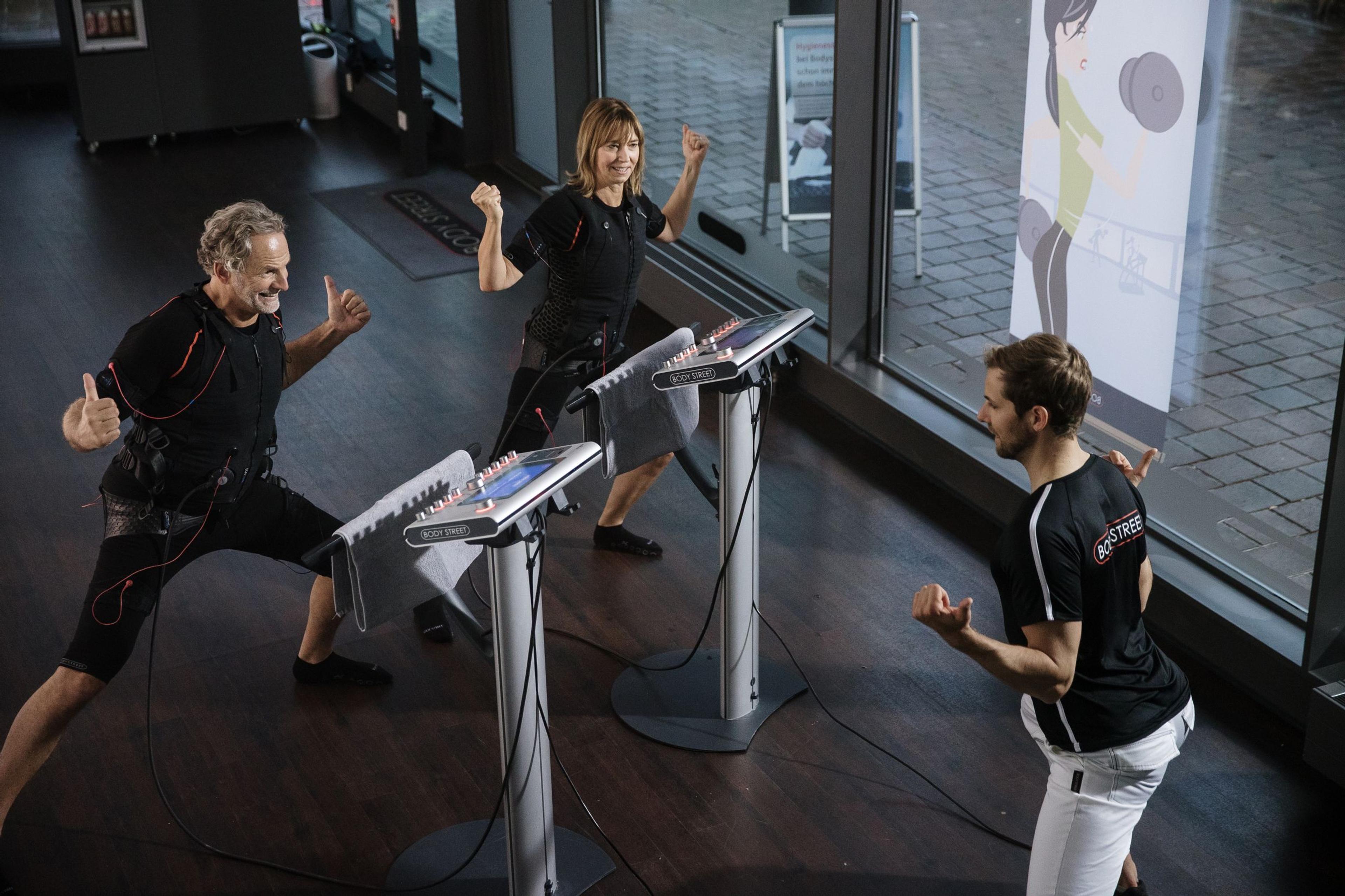 Two adults in EMS training suits exercising with a male instructor.