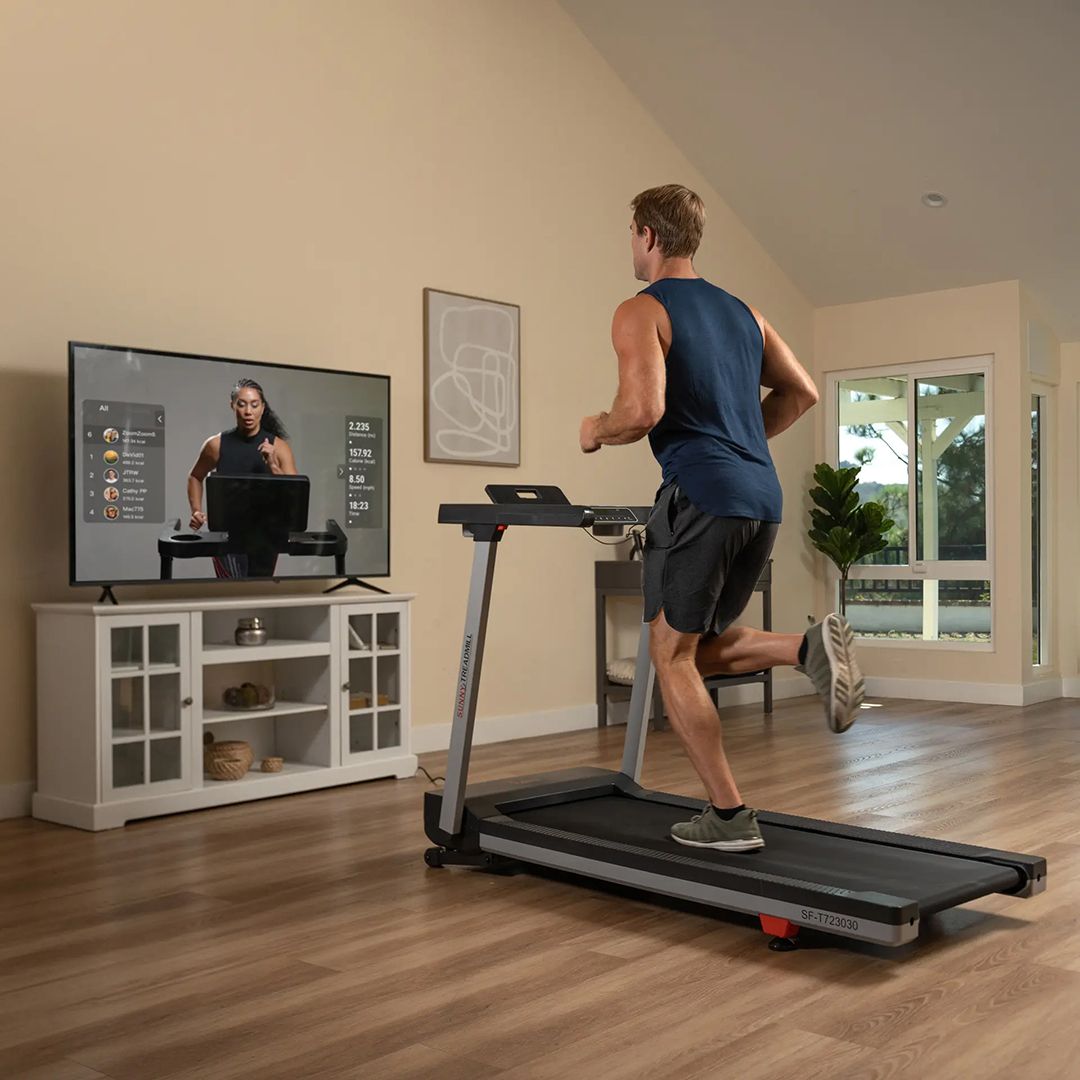Man running on Sunny Health & Fitness treadmill while following guided workout program on television