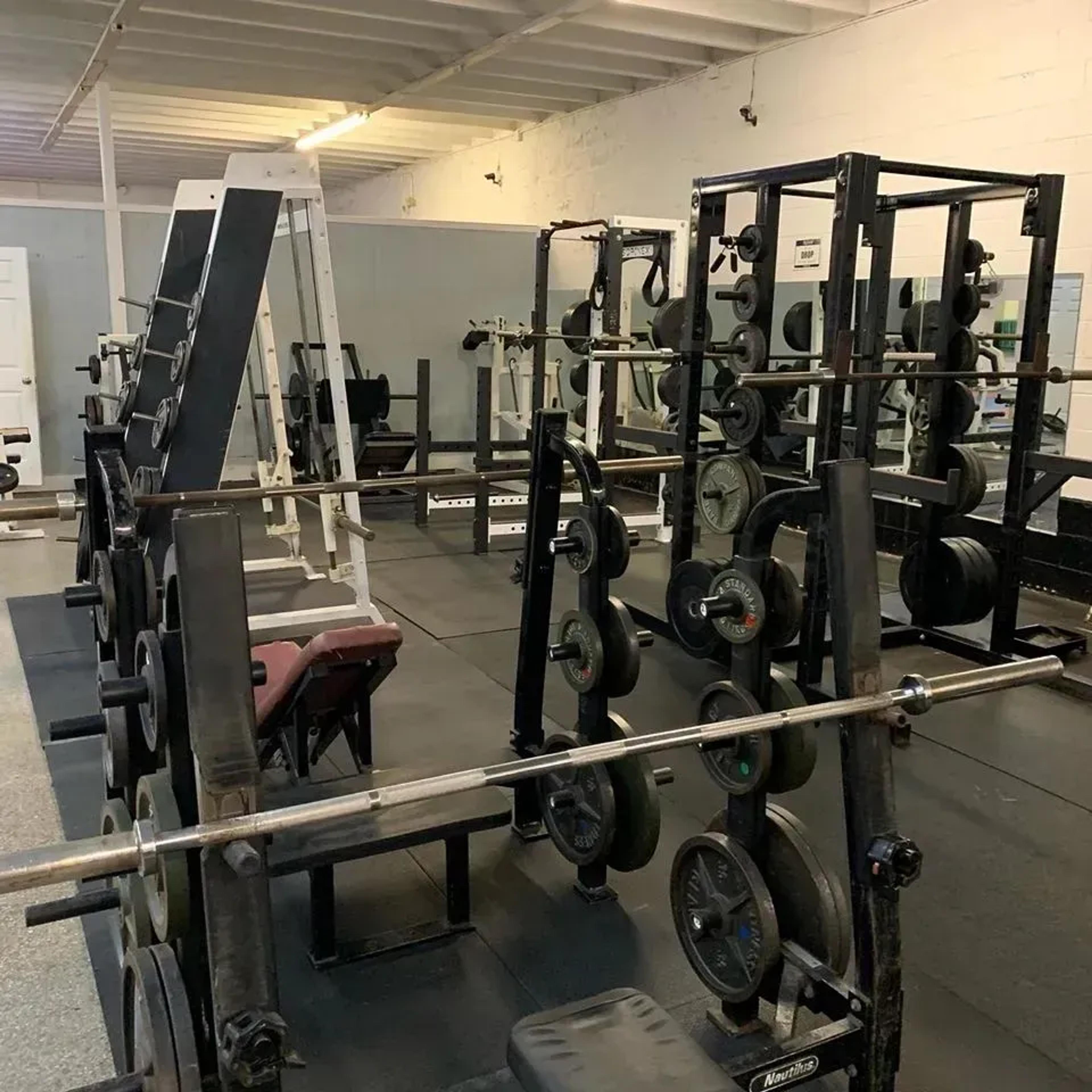 An empty gym with weight racks, barbells, and numerous weight plates.
