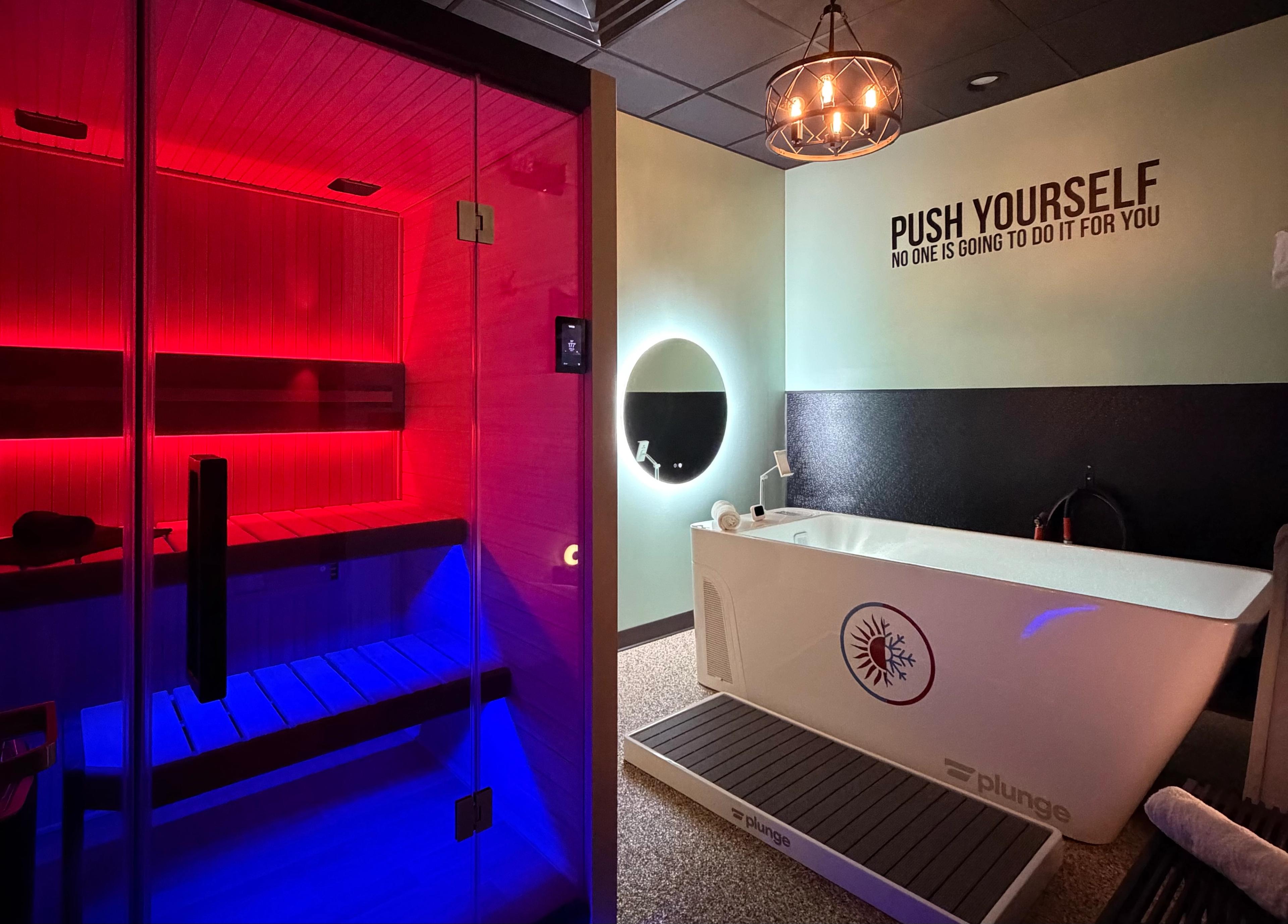 A modern wellness room with an infrared sauna lit in red and blue, and a white Plunge cold plunge tub.