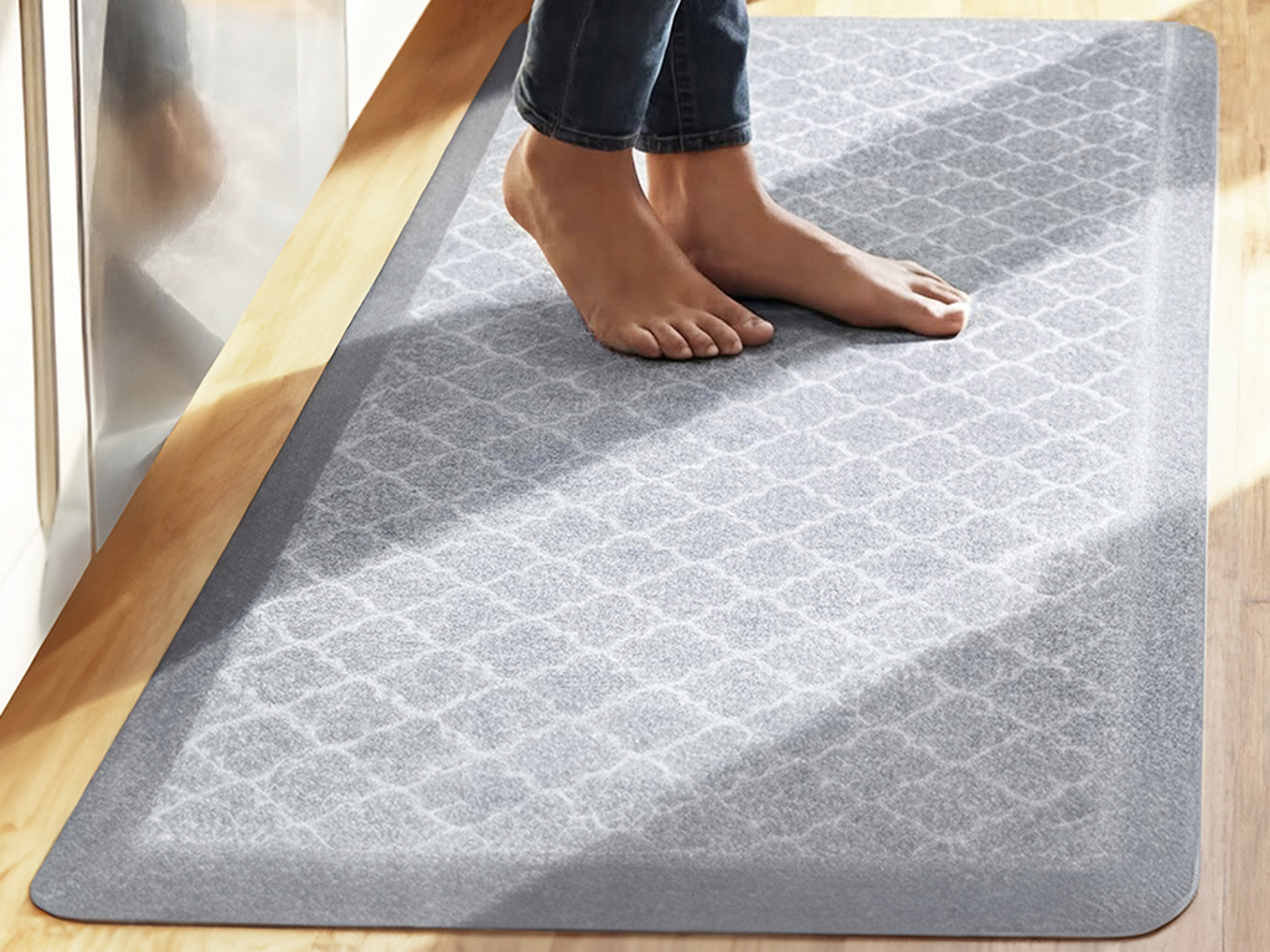 Bare feet standing on a gray patterned mat on a wood floor.