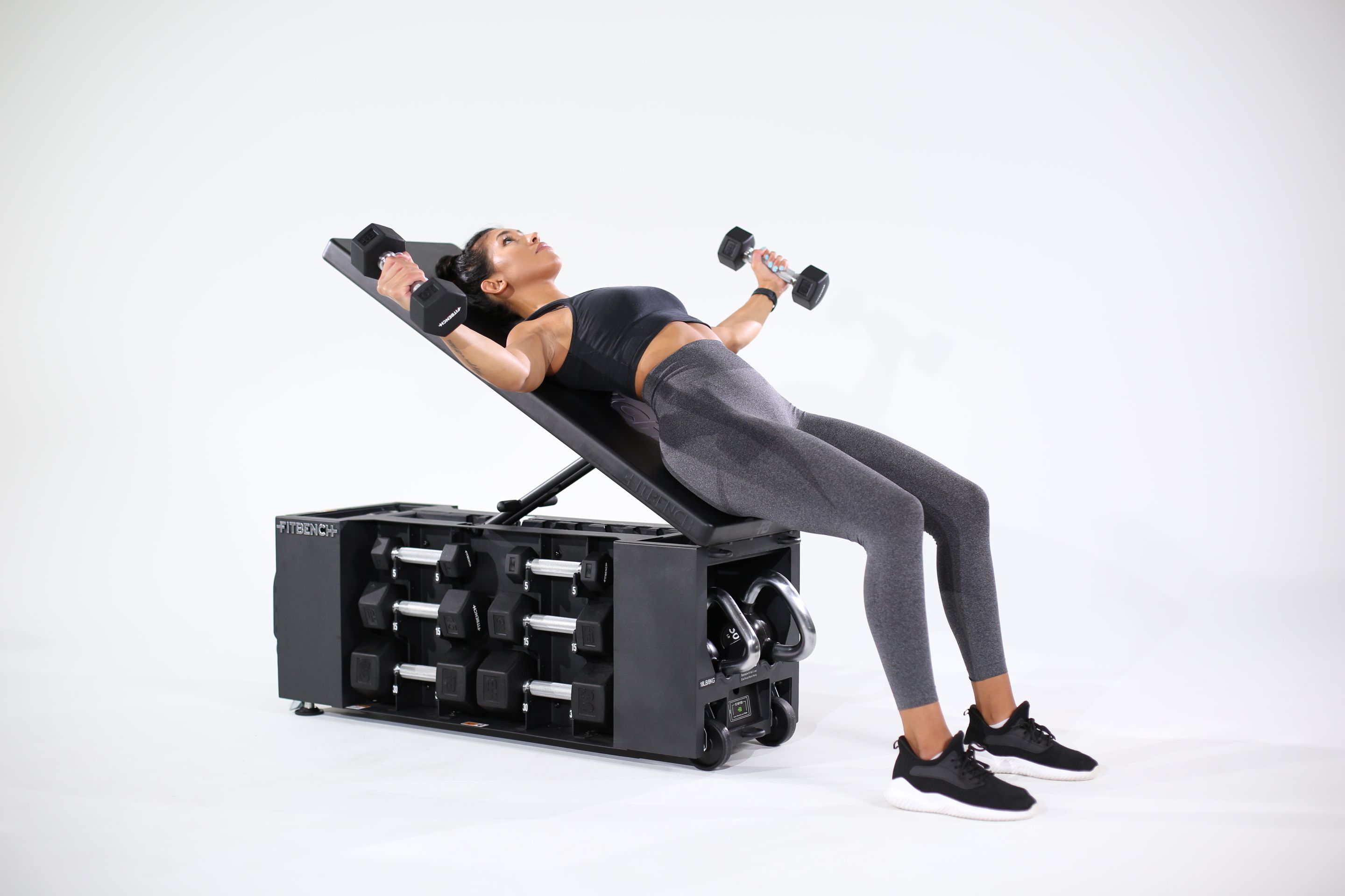 Woman performs dumbbell flyes on an incline bench with integrated storage.