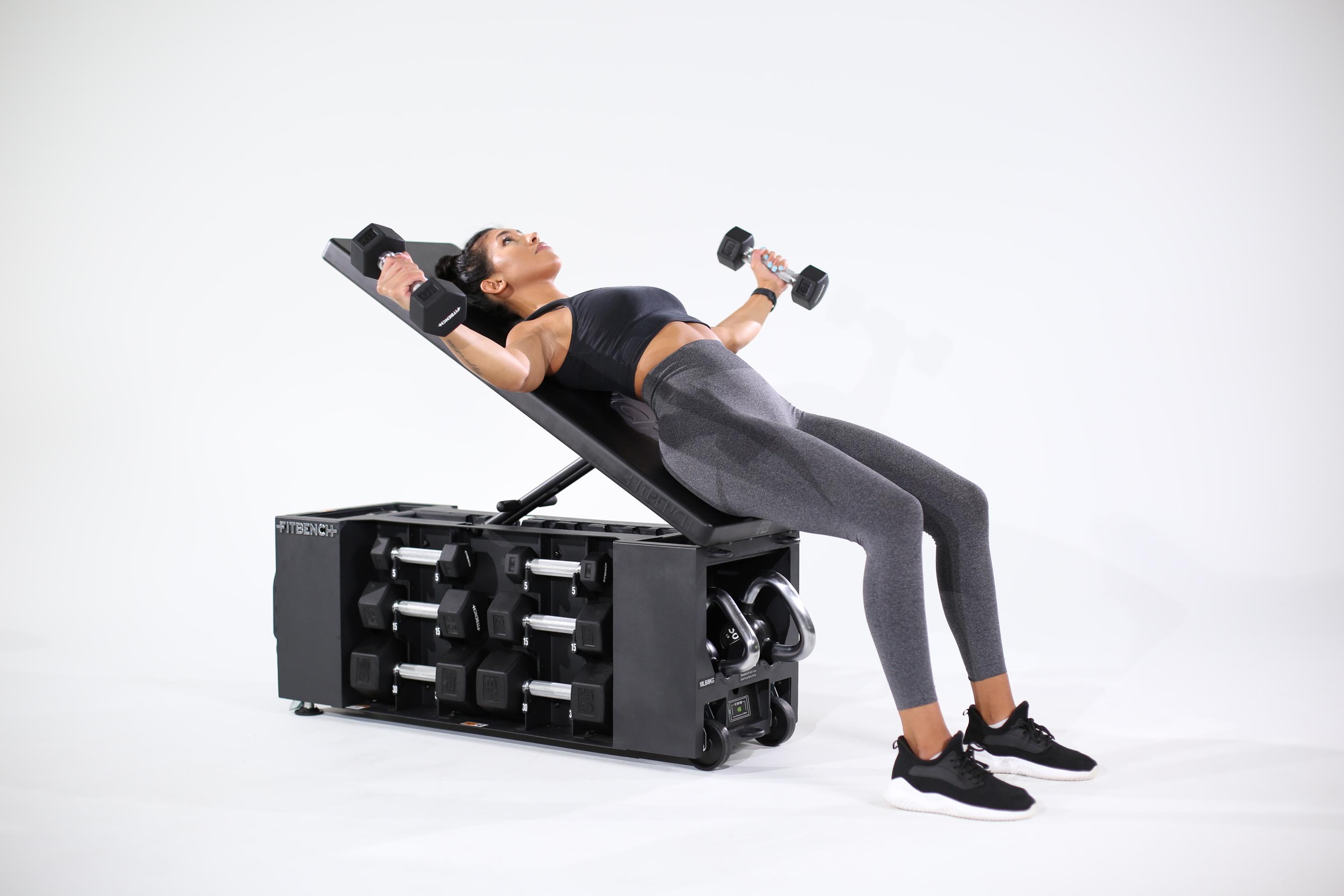 Woman performs dumbbell flyes on an incline bench with integrated storage.