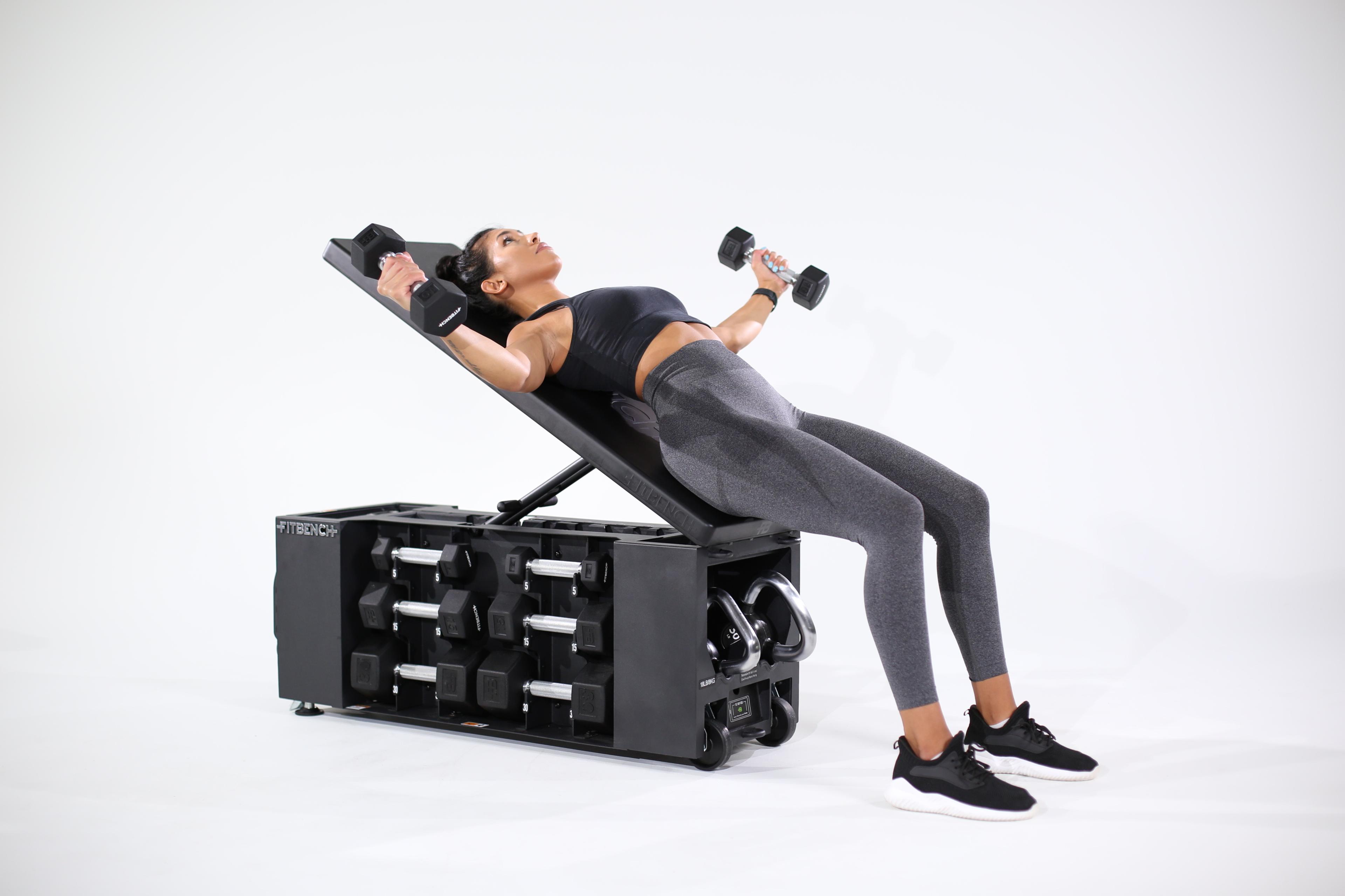 Woman performs dumbbell flyes on an incline bench with integrated storage.