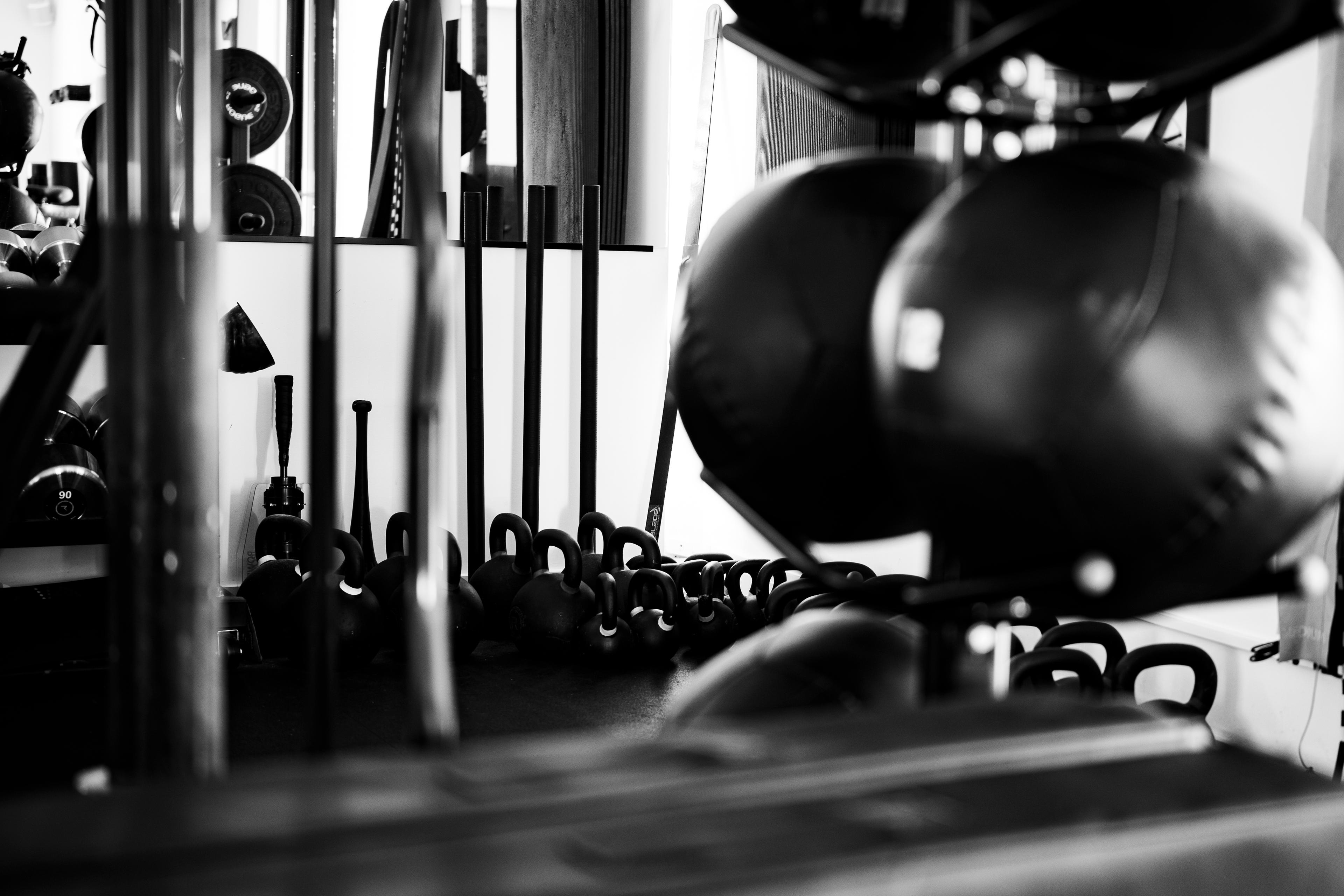 Black and white photo of a gym with medicine balls, kettlebells, and other fitness equipment.
