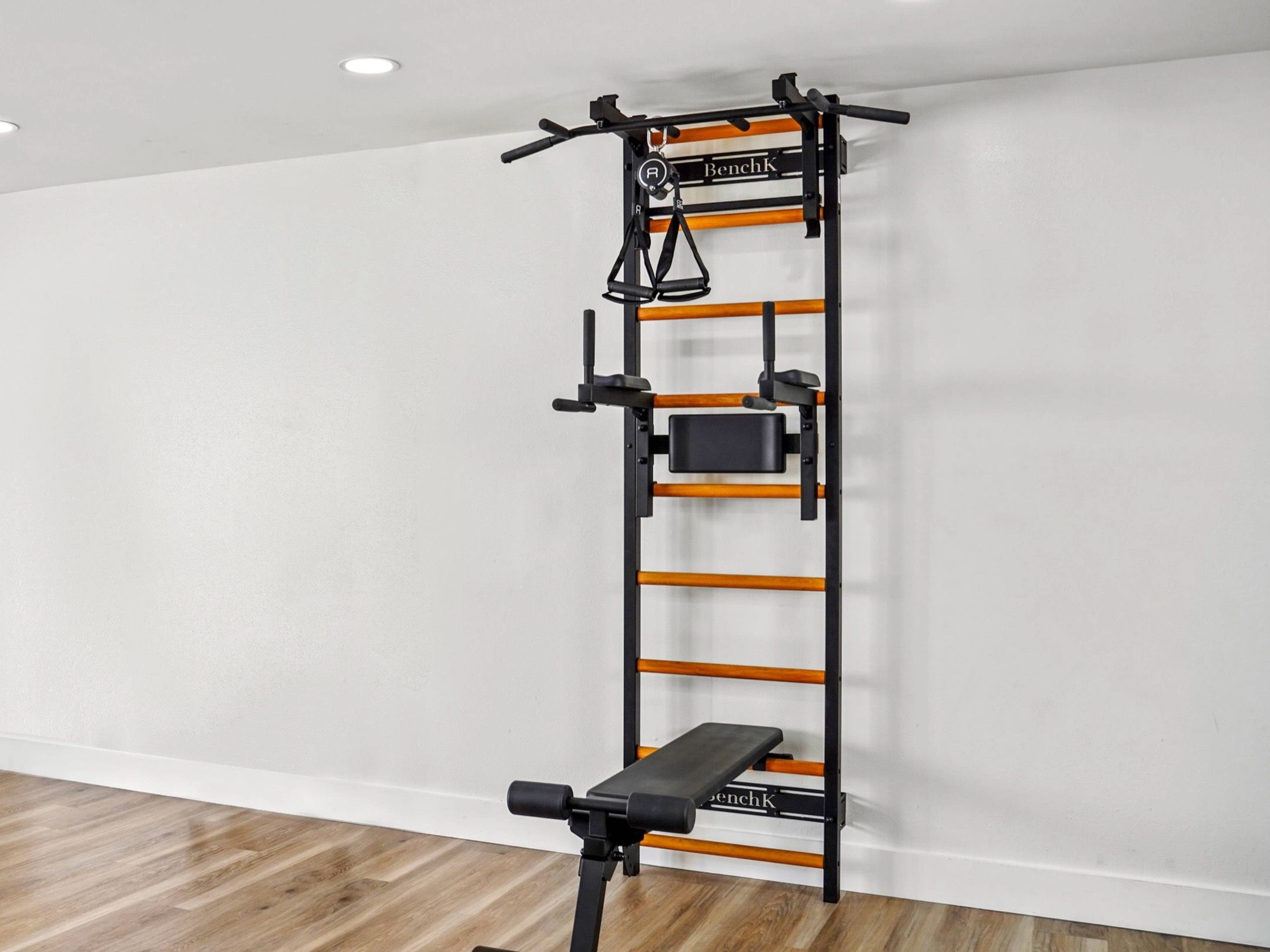 BenchK wall-mounted fitness system with a Swedish ladder, pull-up bar, dip station, and workout bench.