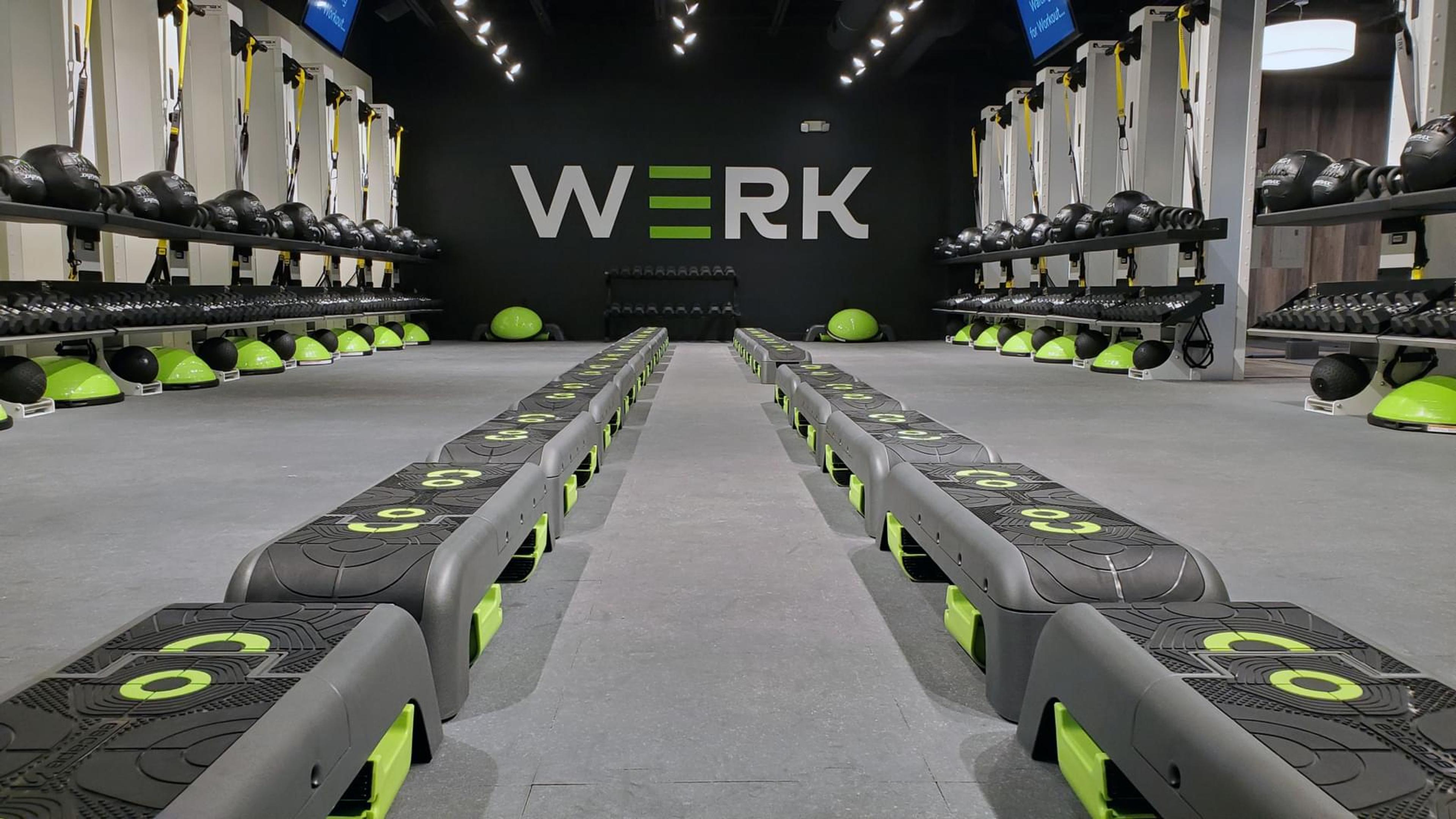 A WERK gym with two long rows of fitness steps and wall-mounted equipment like dumbbells and kettlebells.
