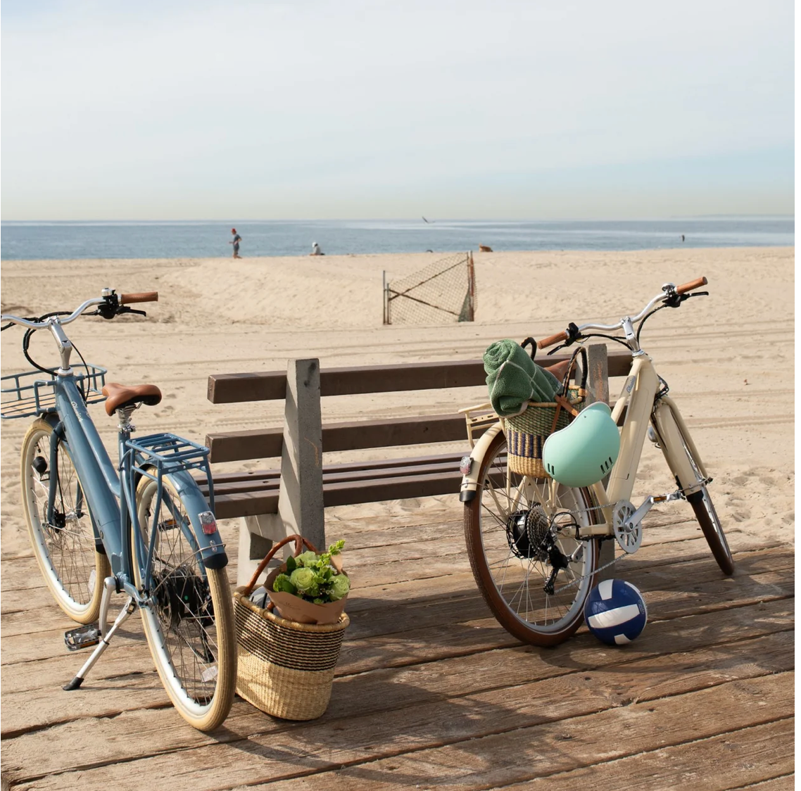 Blue e-bike with a front basket, rear rack, brown saddle, and white tires.