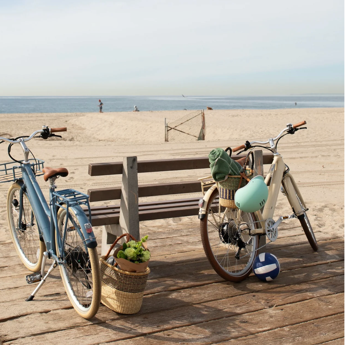 Blue e-bike with a front basket, rear rack, brown saddle, and white tires.
