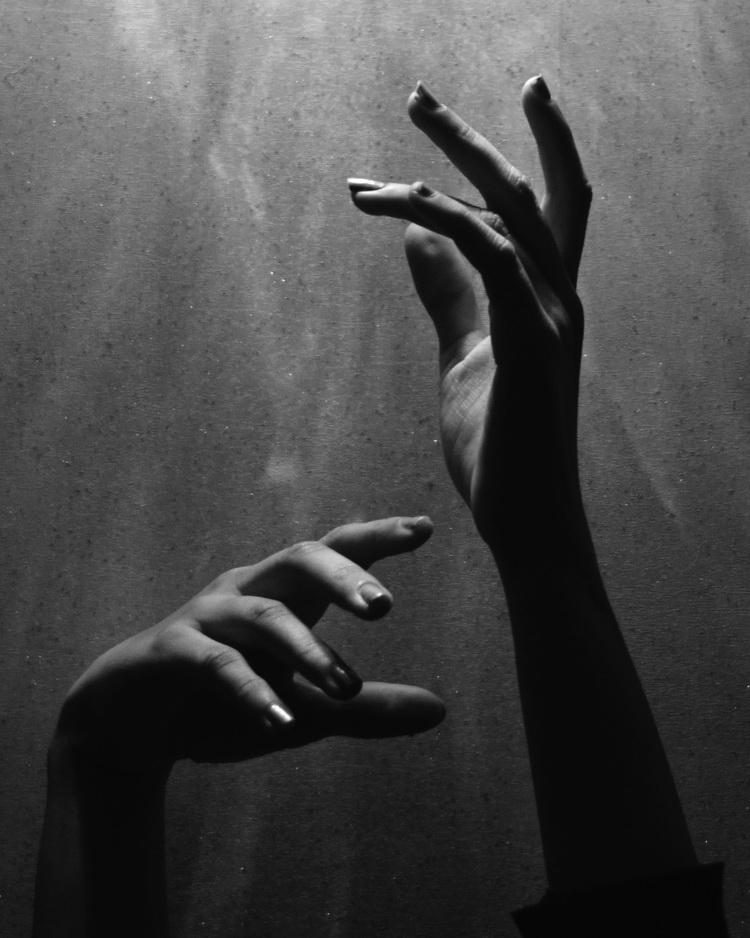 Two dramatically lit hands in black and white against a textured background; one reaches up, the other is curved.