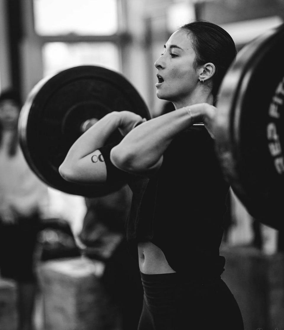 Black and white photo of a woman holding a barbell in a front rack position.
