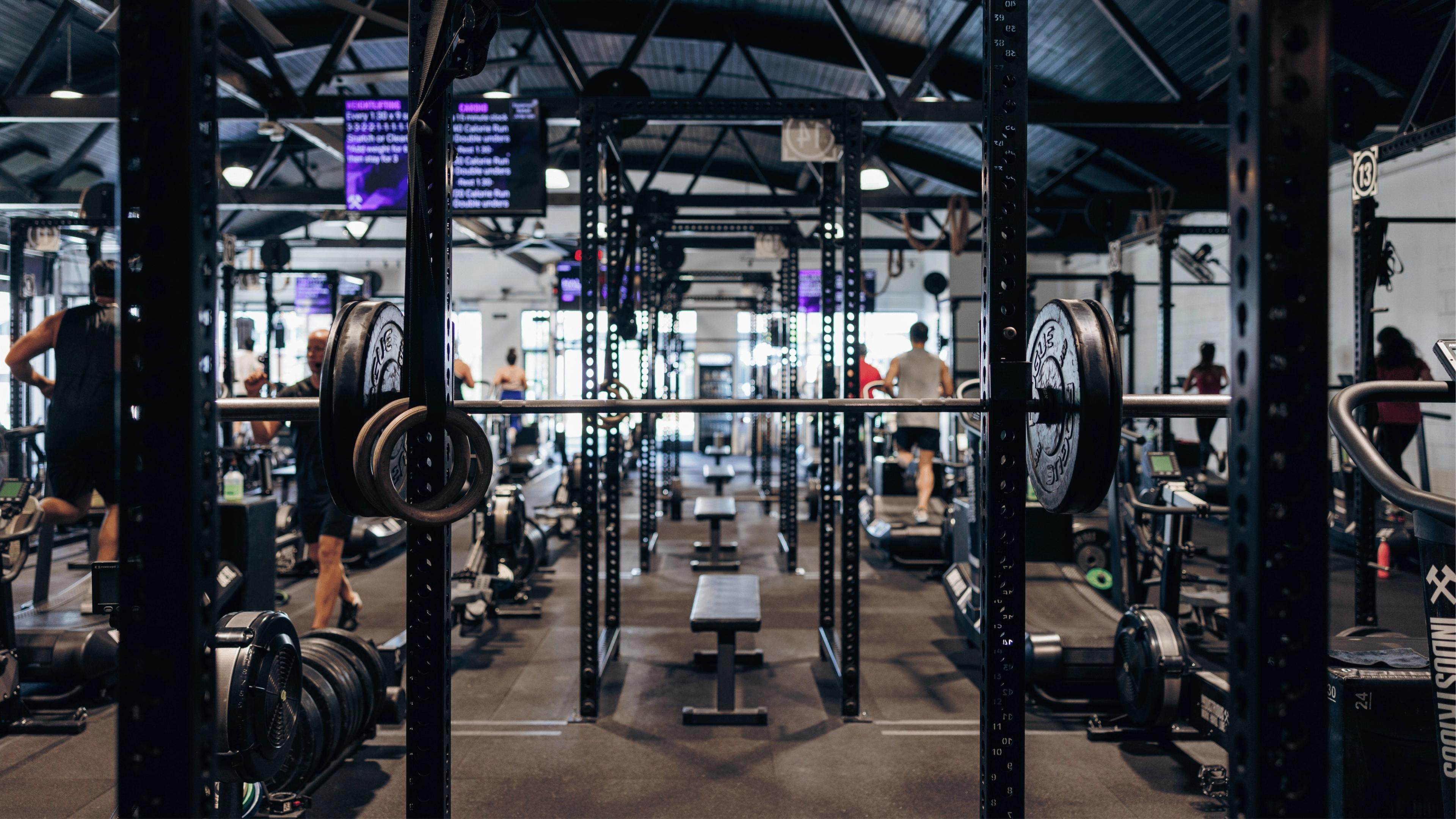 A modern gym interior with people exercising on various fitness equipment.
