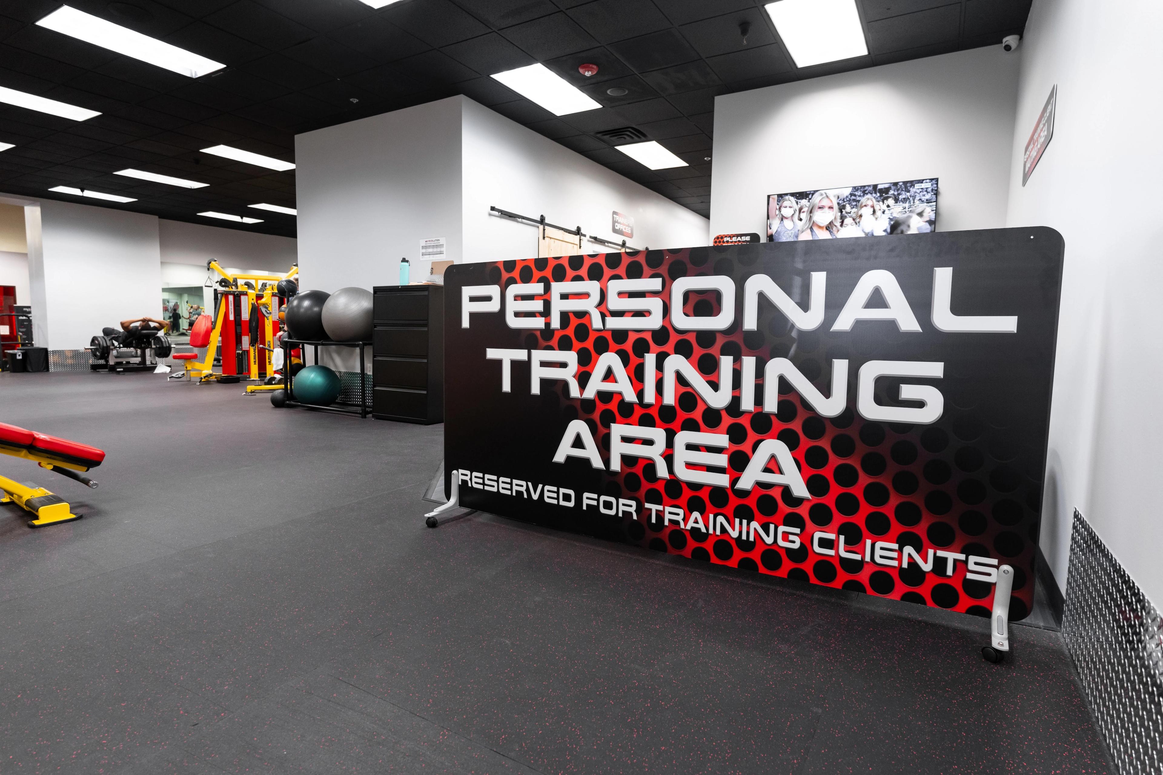 A gym interior with a black and red sign reading "Personal Training Area" and fitness equipment in the background.