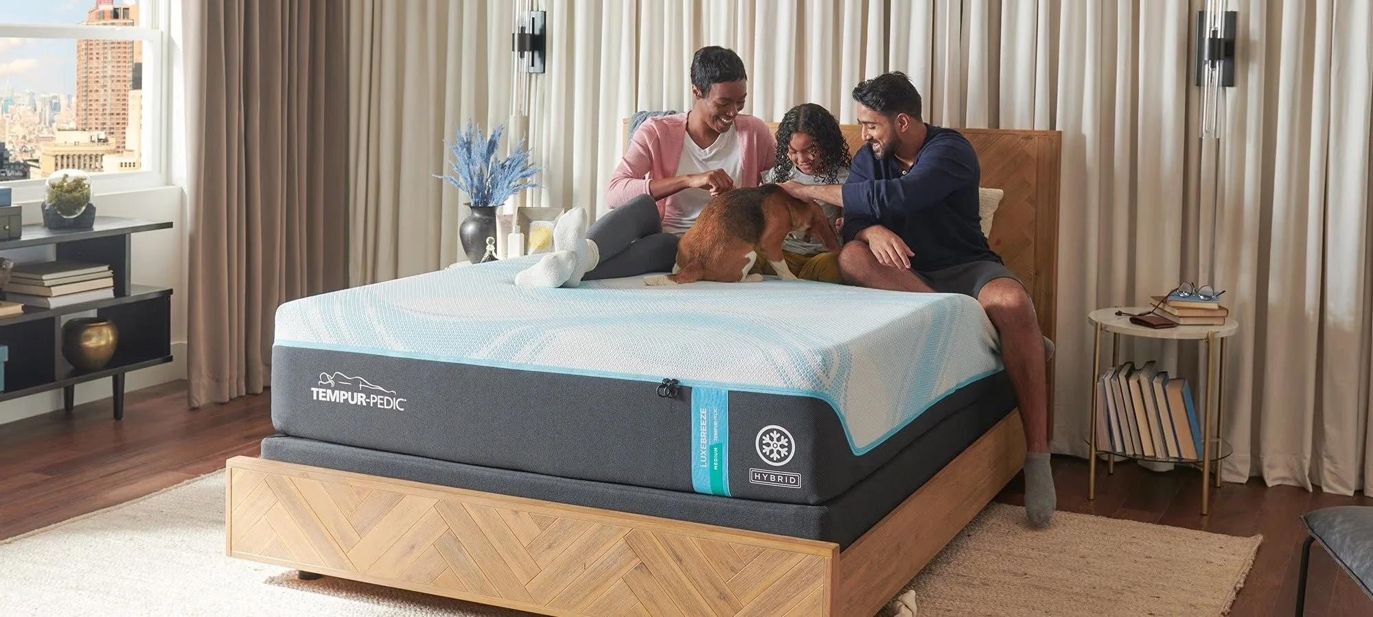 A family of three and their dog sit on a Tempur-Pedic mattress in a bedroom.