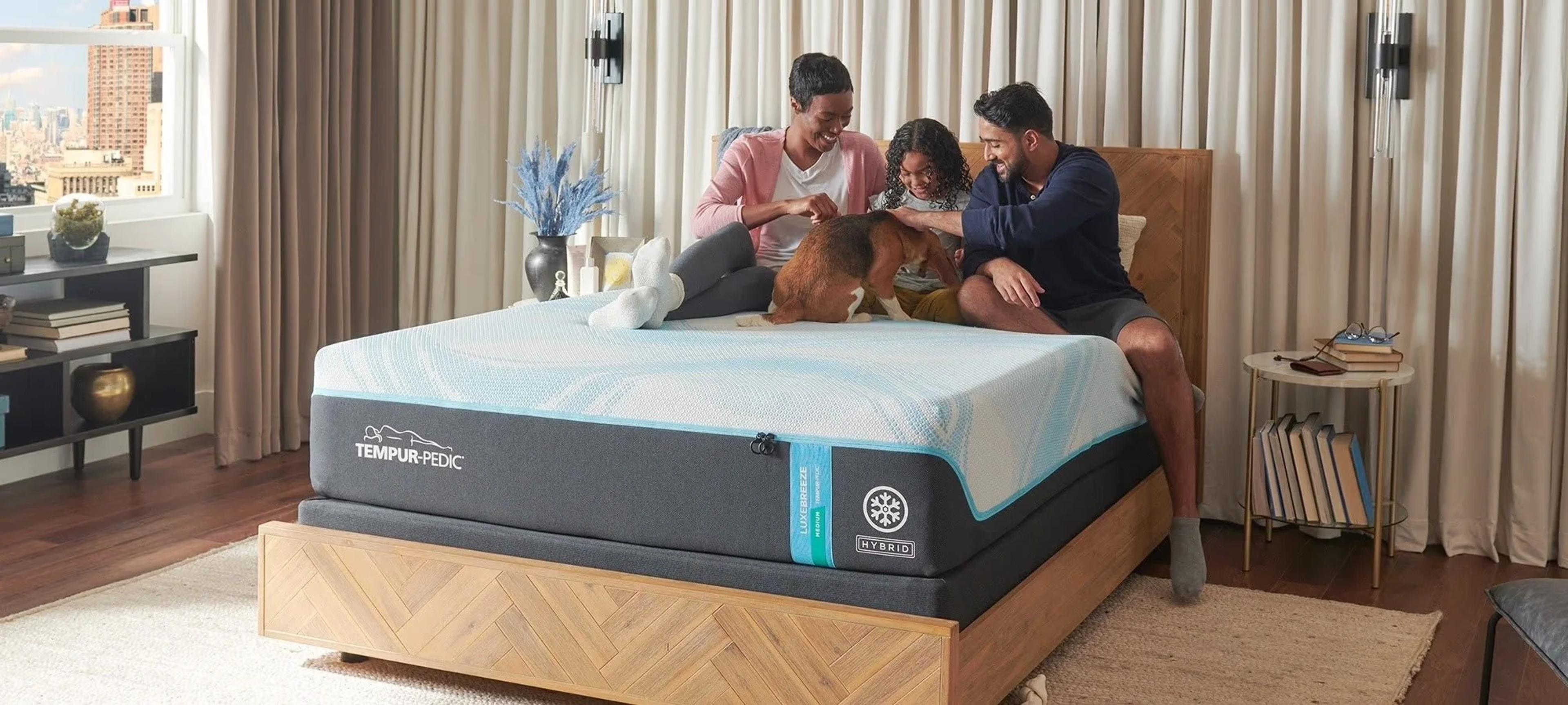A family of three and their dog sit on a Tempur-Pedic mattress in a bedroom.
