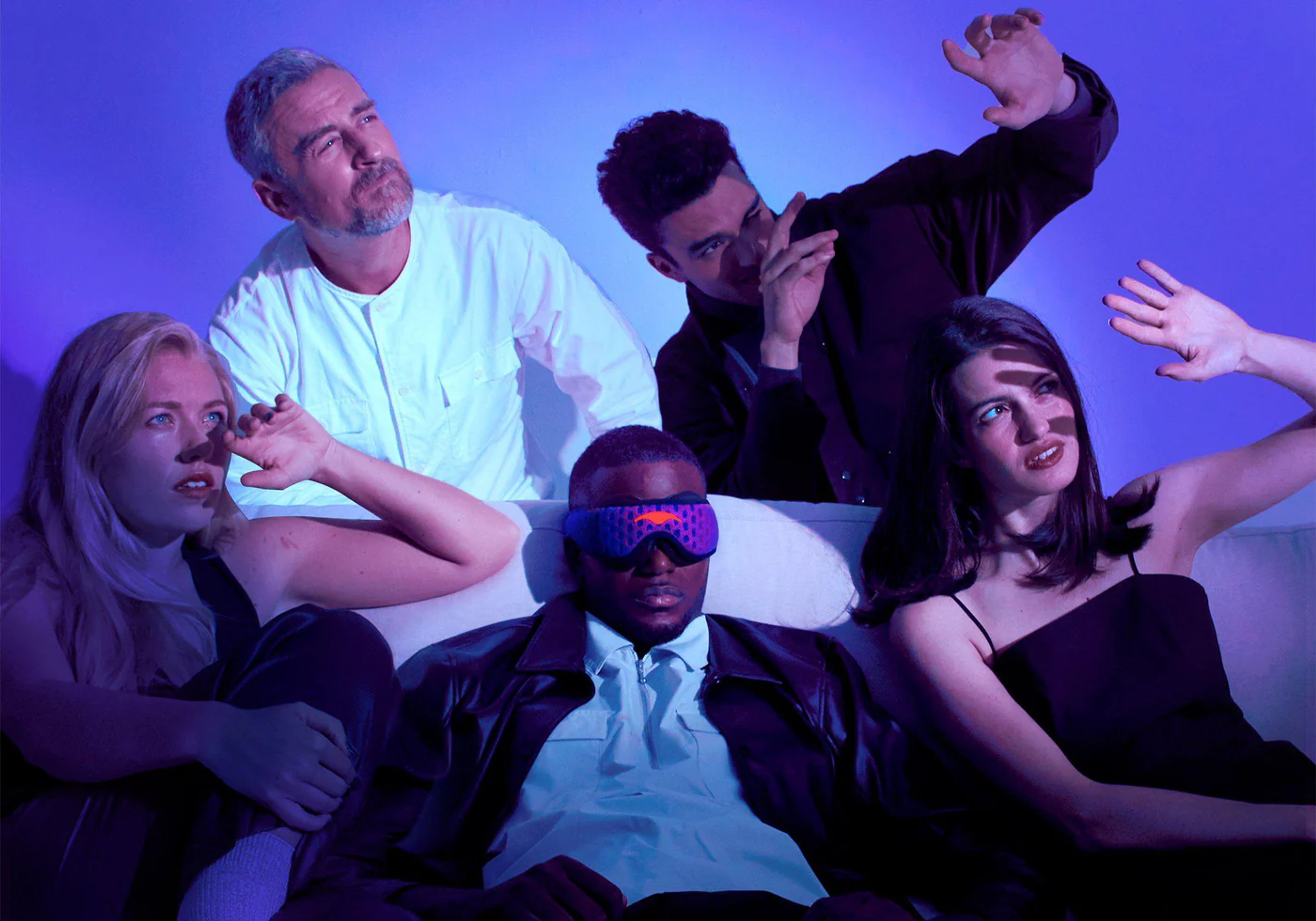 Five people on a couch; one man wears a futuristic eye mask, while others react to a dramatic purple light.